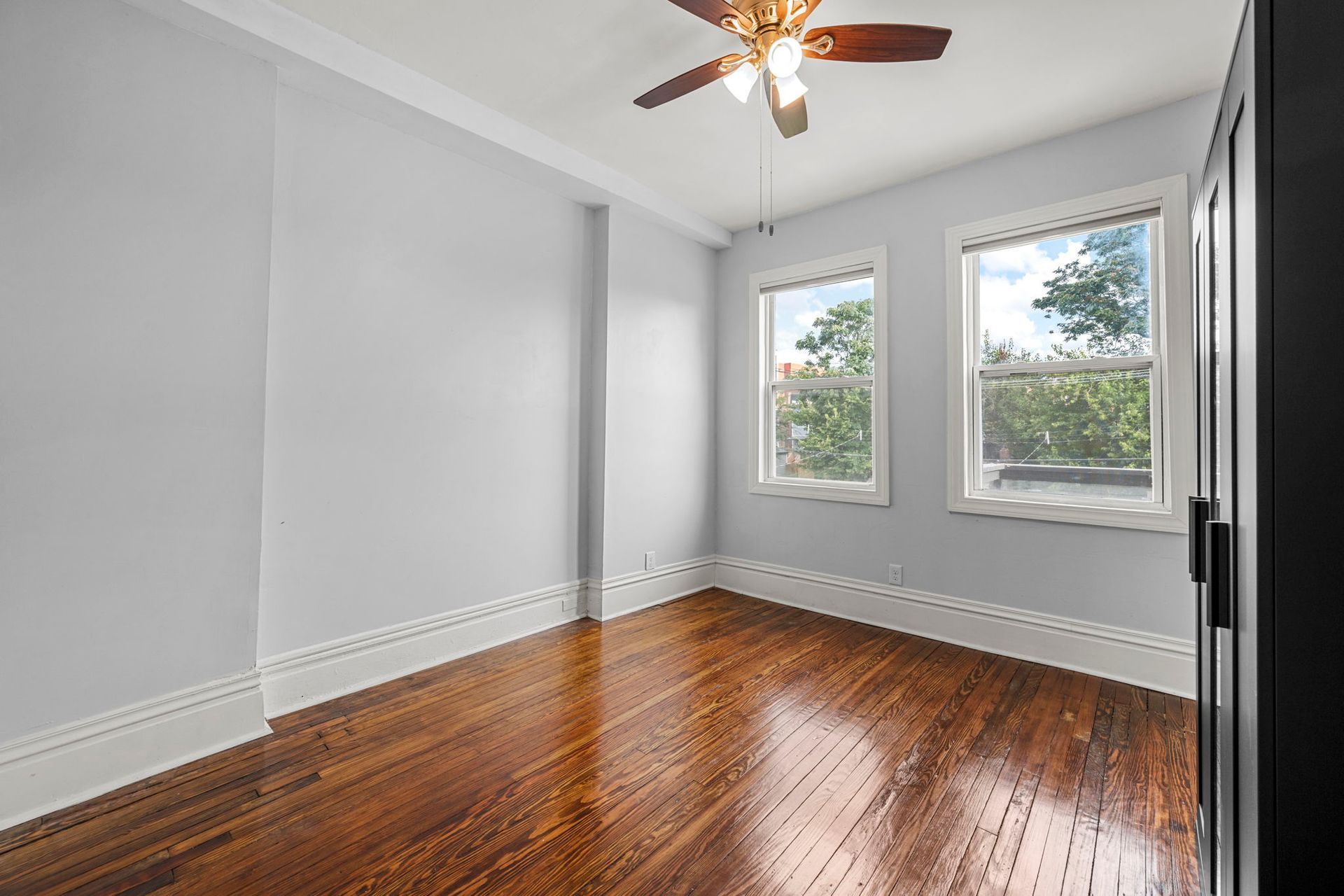 Empty room with hardwood floors, two windows, and a ceiling fan.