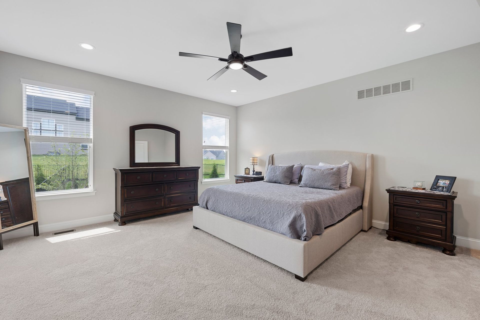 A bedroom with a bed , dresser , mirror and ceiling fan.