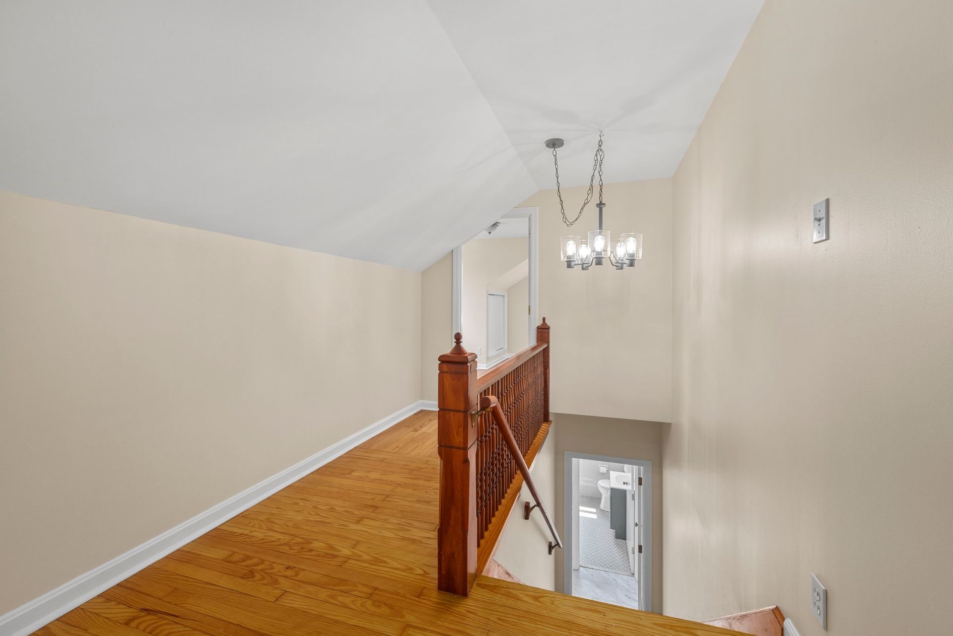 An empty hallway with stairs and a chandelier hanging from the ceiling.