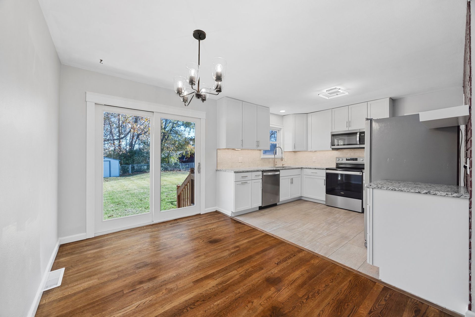 An empty kitchen with hardwood floors and white cabinets.