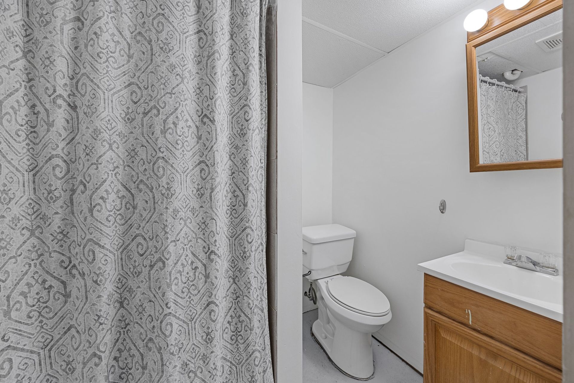 A bathroom with a toilet , sink , mirror and shower curtain.