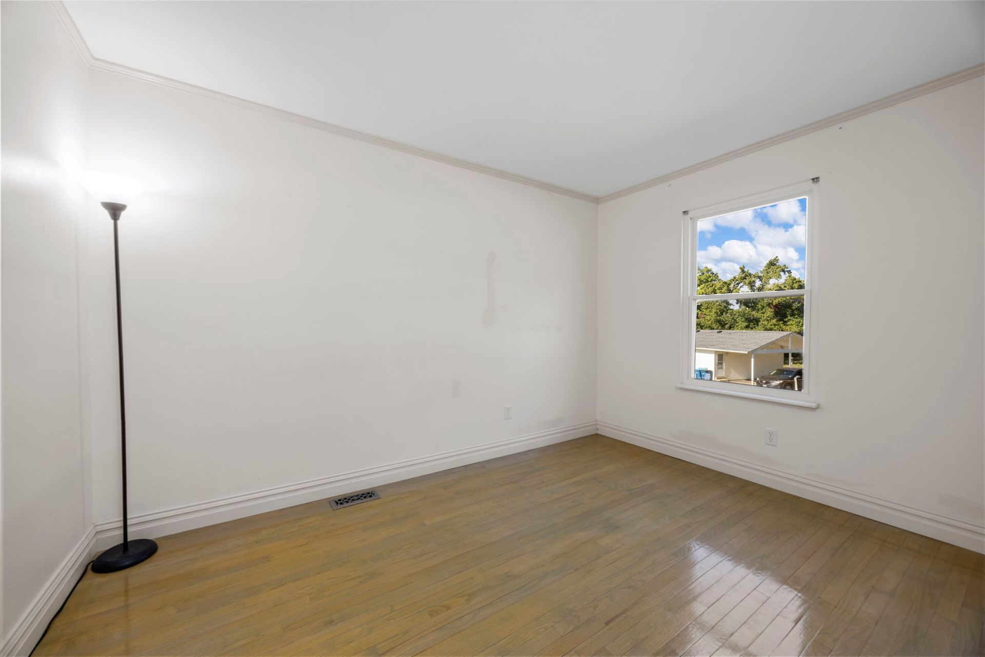 Empty room with hardwood floor, window, and floor lamp.