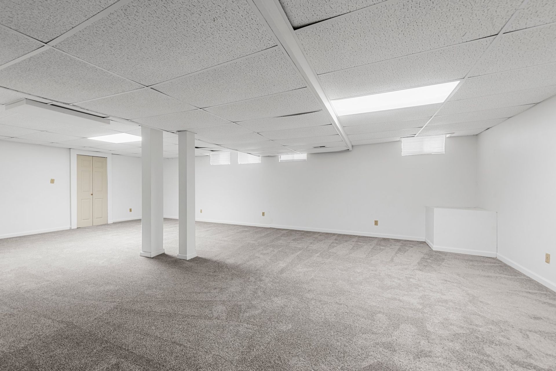 An empty basement with a carpeted floor and white walls.