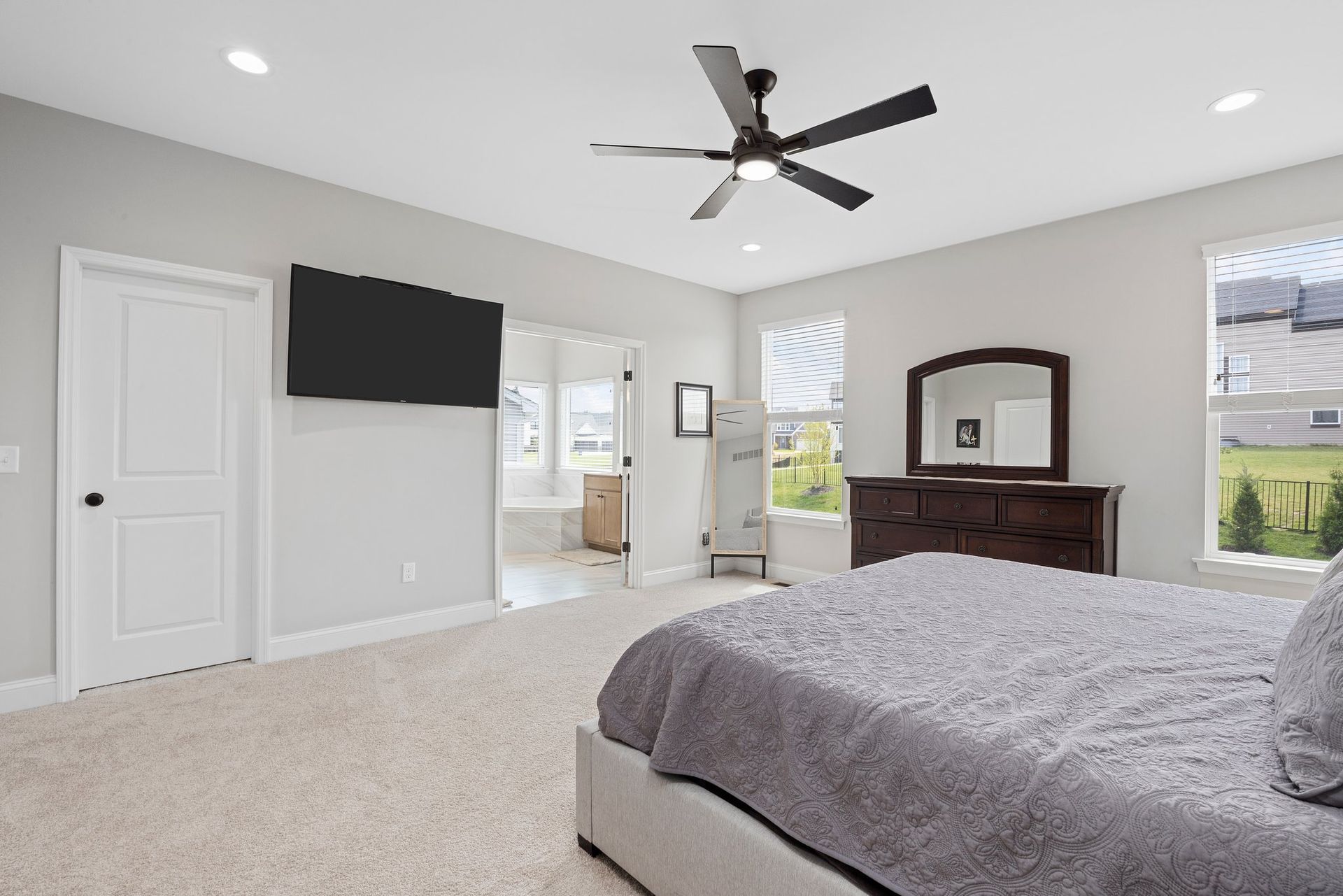 A bedroom with a bed , dresser , television and ceiling fan.