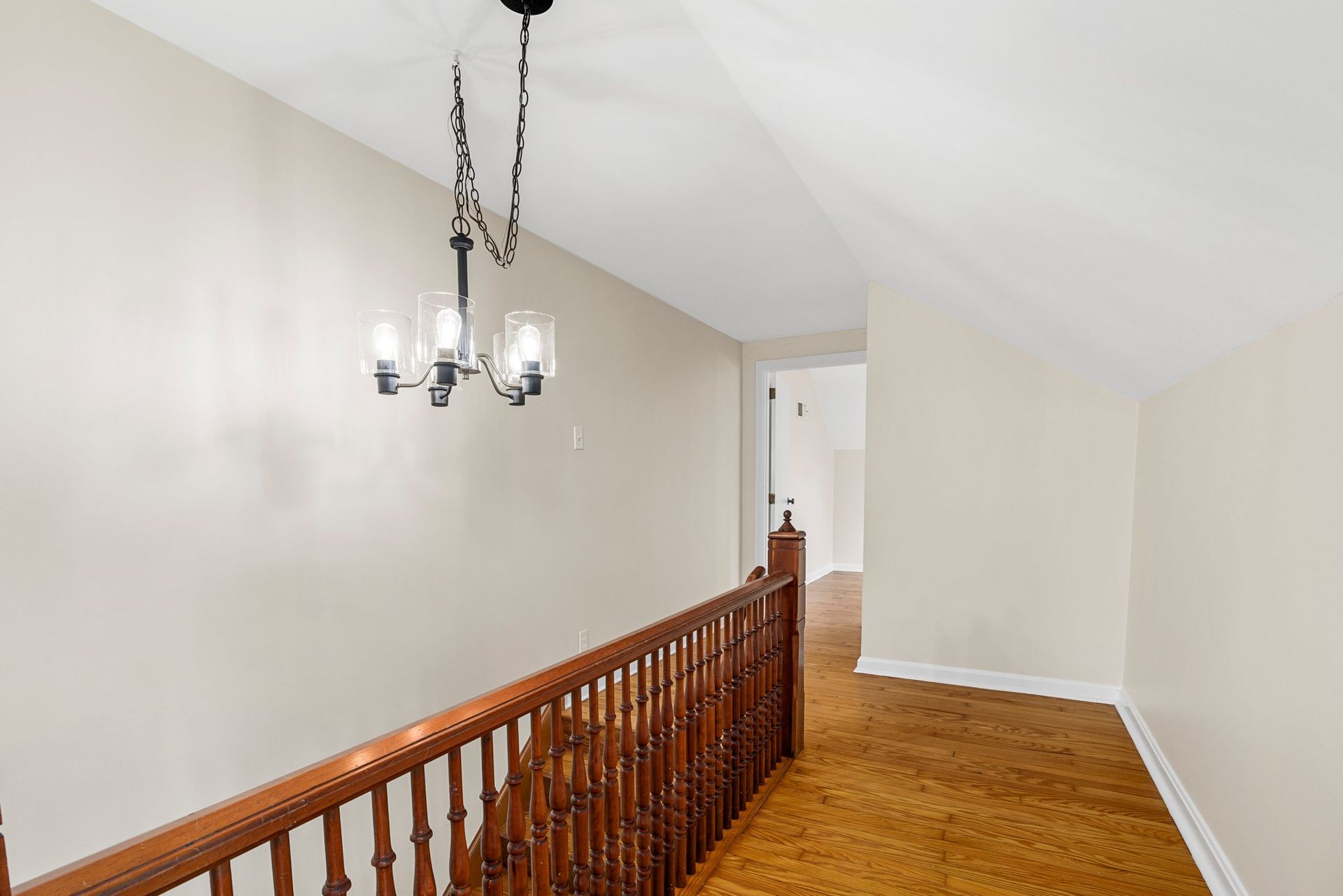 A hallway with a wooden railing and a chandelier hanging from the ceiling.