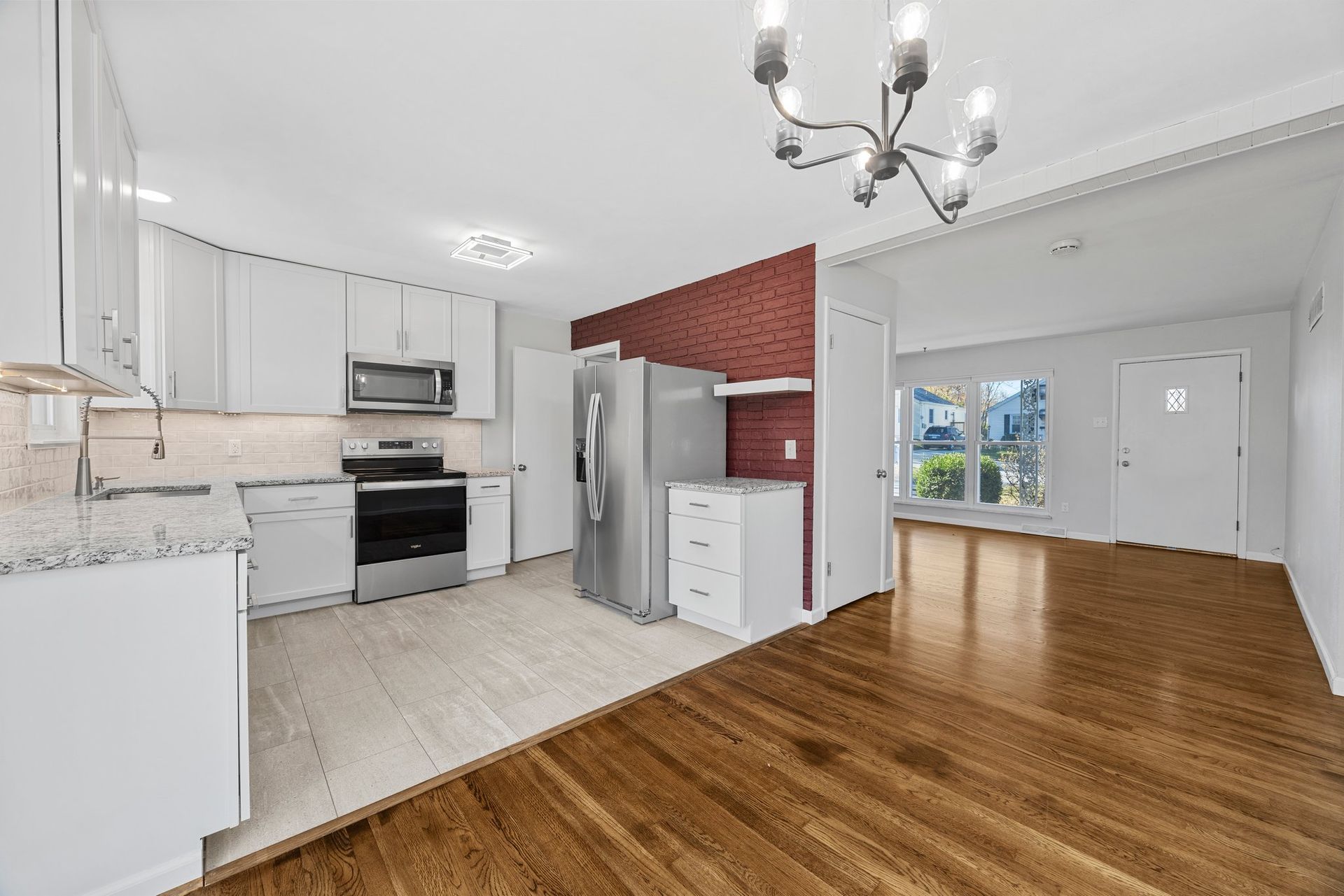 An empty kitchen with hardwood floors , white cabinets , stainless steel appliances and a refrigerator.
