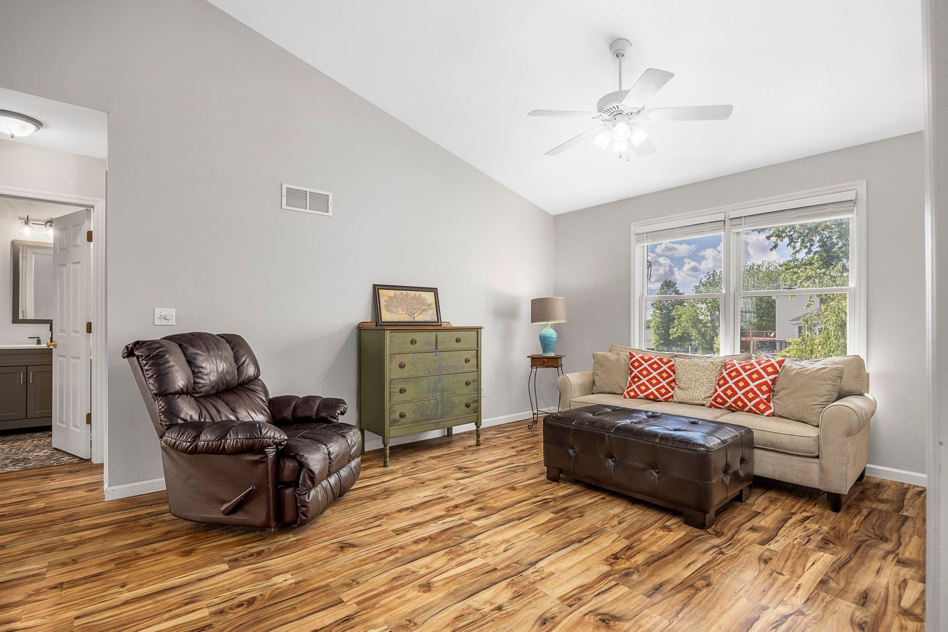 A living room with a couch , chair , ottoman and ceiling fan.