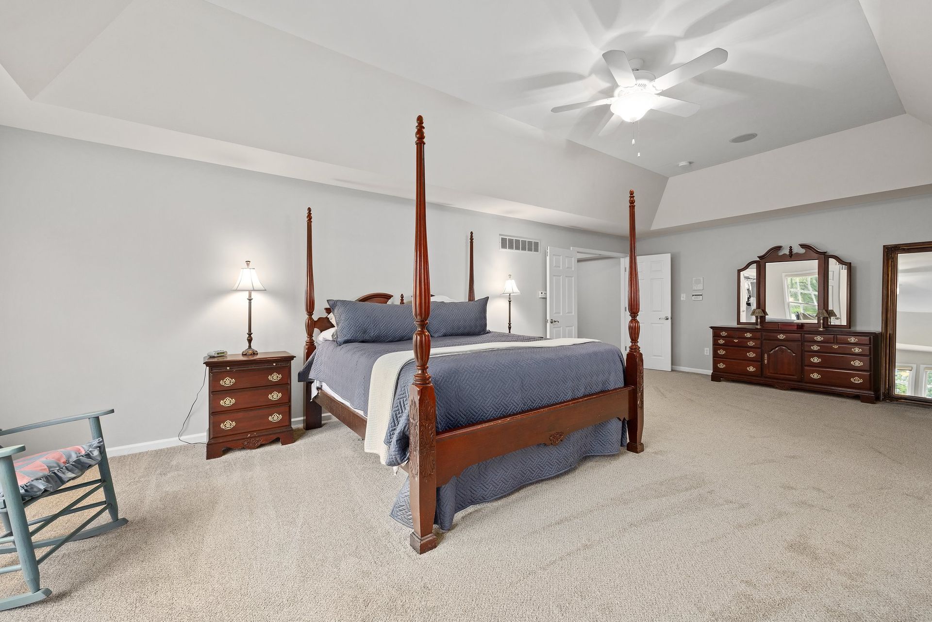 A bedroom with a four poster bed , dresser , nightstand , mirror and ceiling fan.