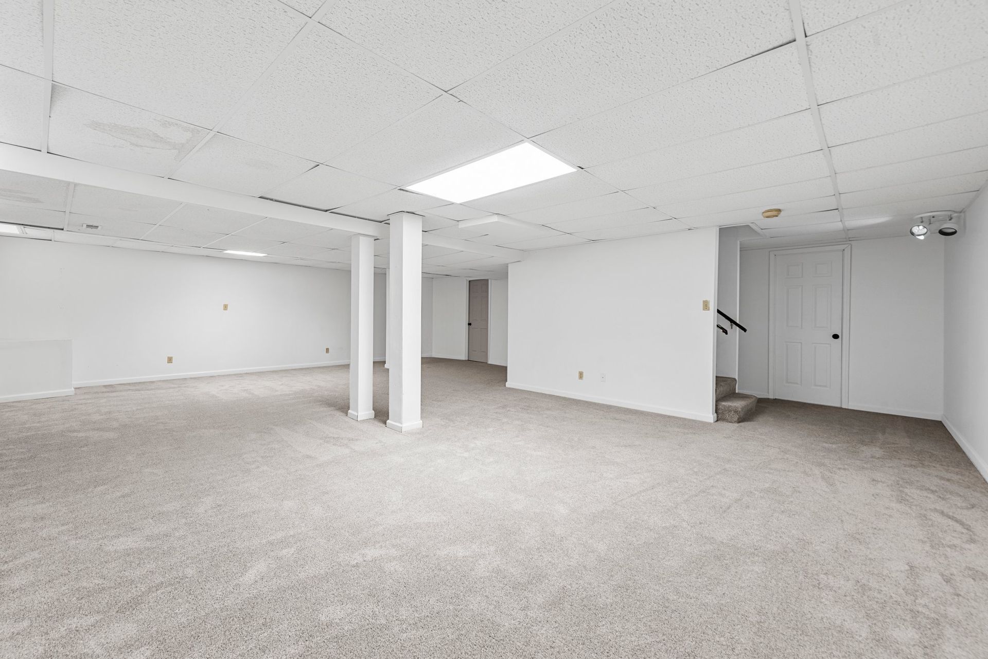 An empty basement with a carpeted floor and white walls.