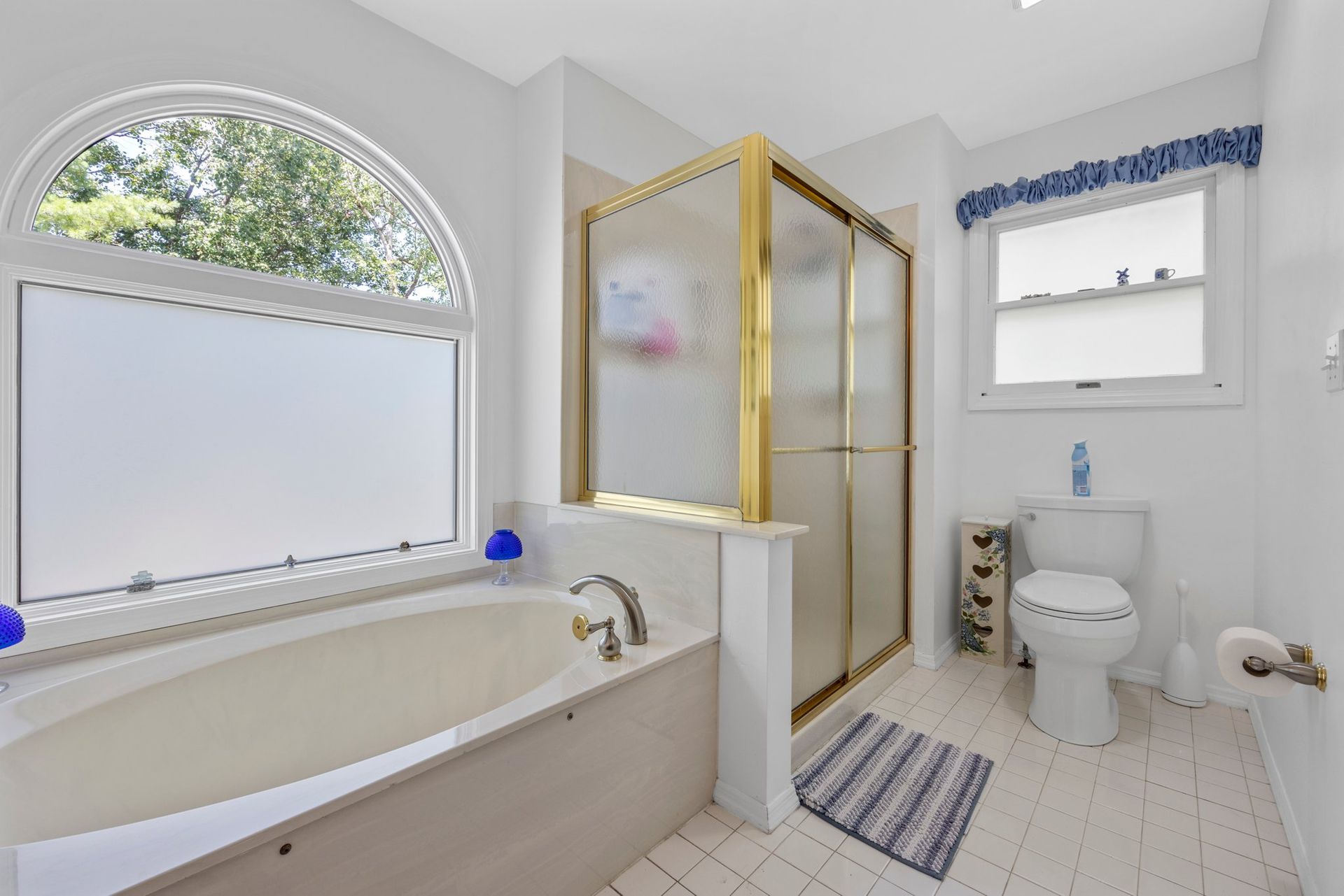 A bathroom with a tub , toilet , shower and window.