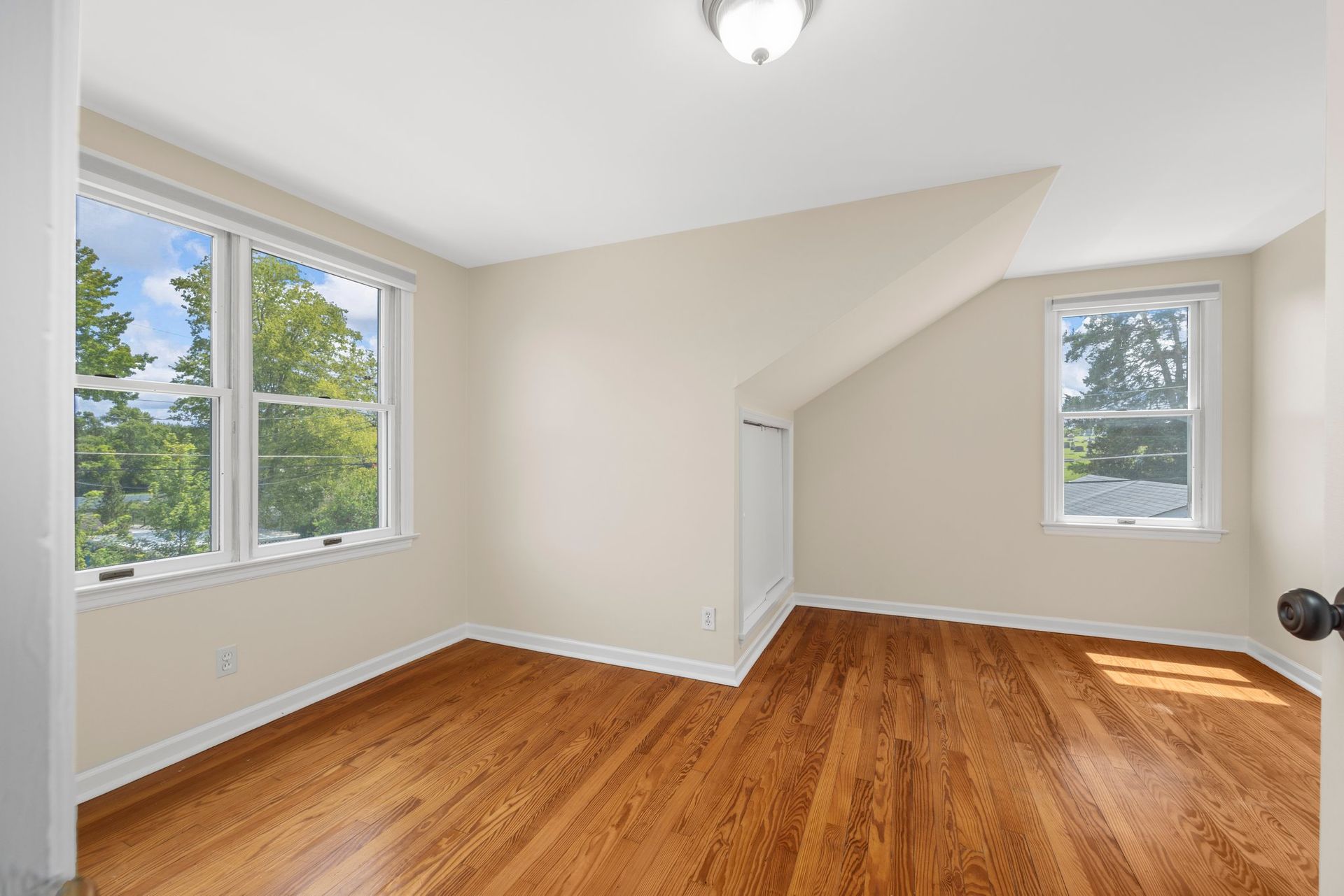 An empty room with hardwood floors and two windows.