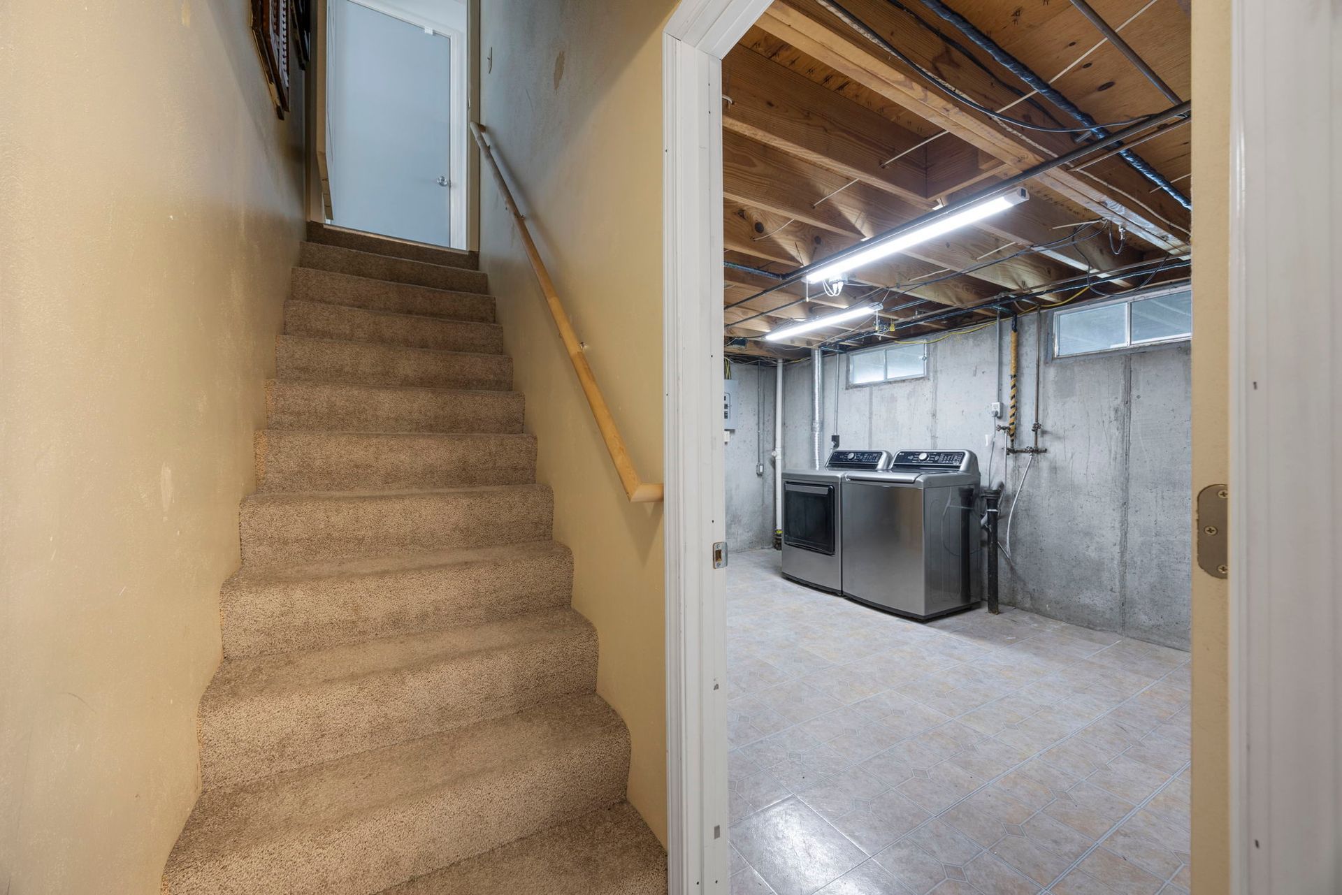 Staircase leading down to a basement laundry room with concrete walls and a large, metallic washer and dryer.
