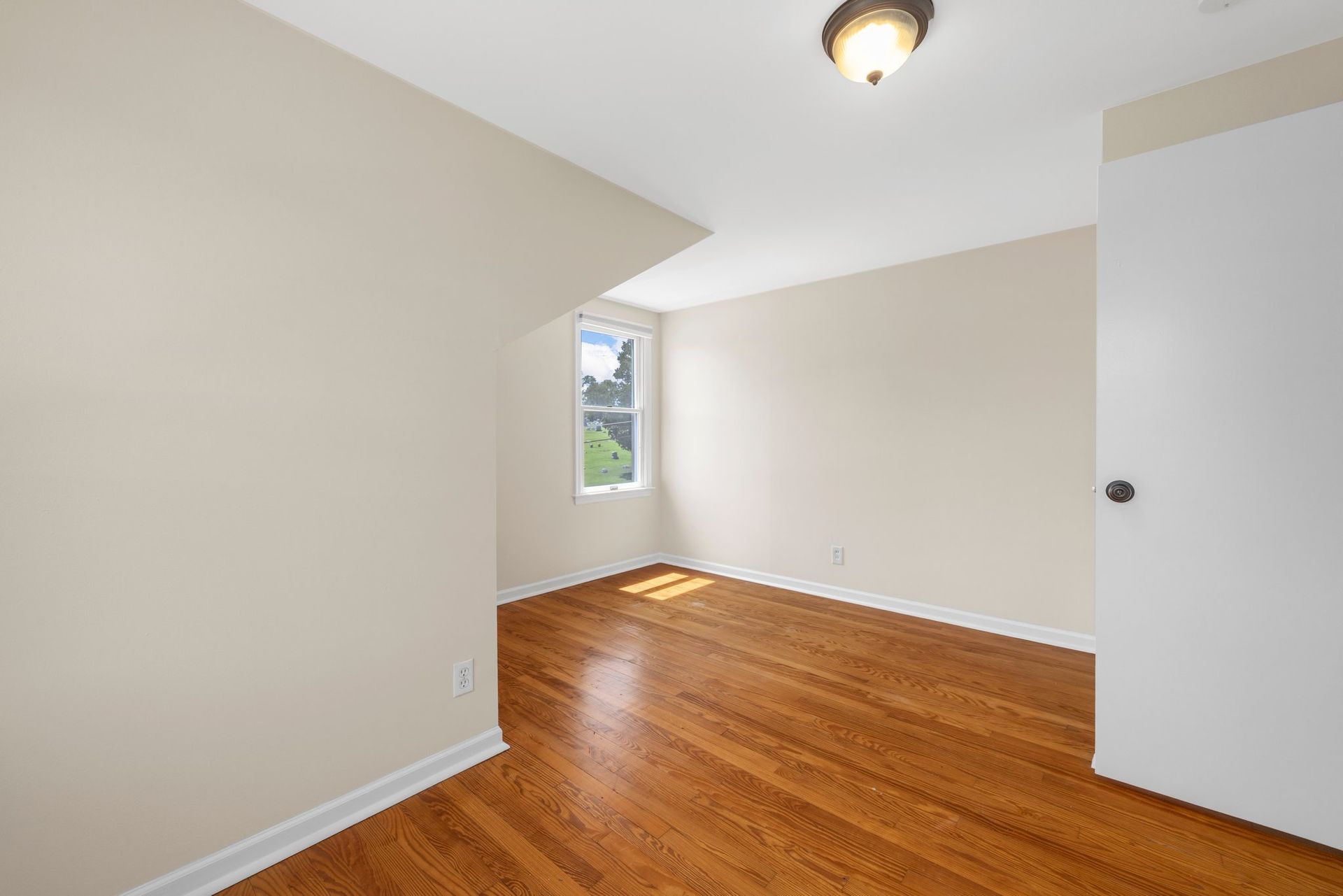 An empty bedroom with hardwood floors and white walls.