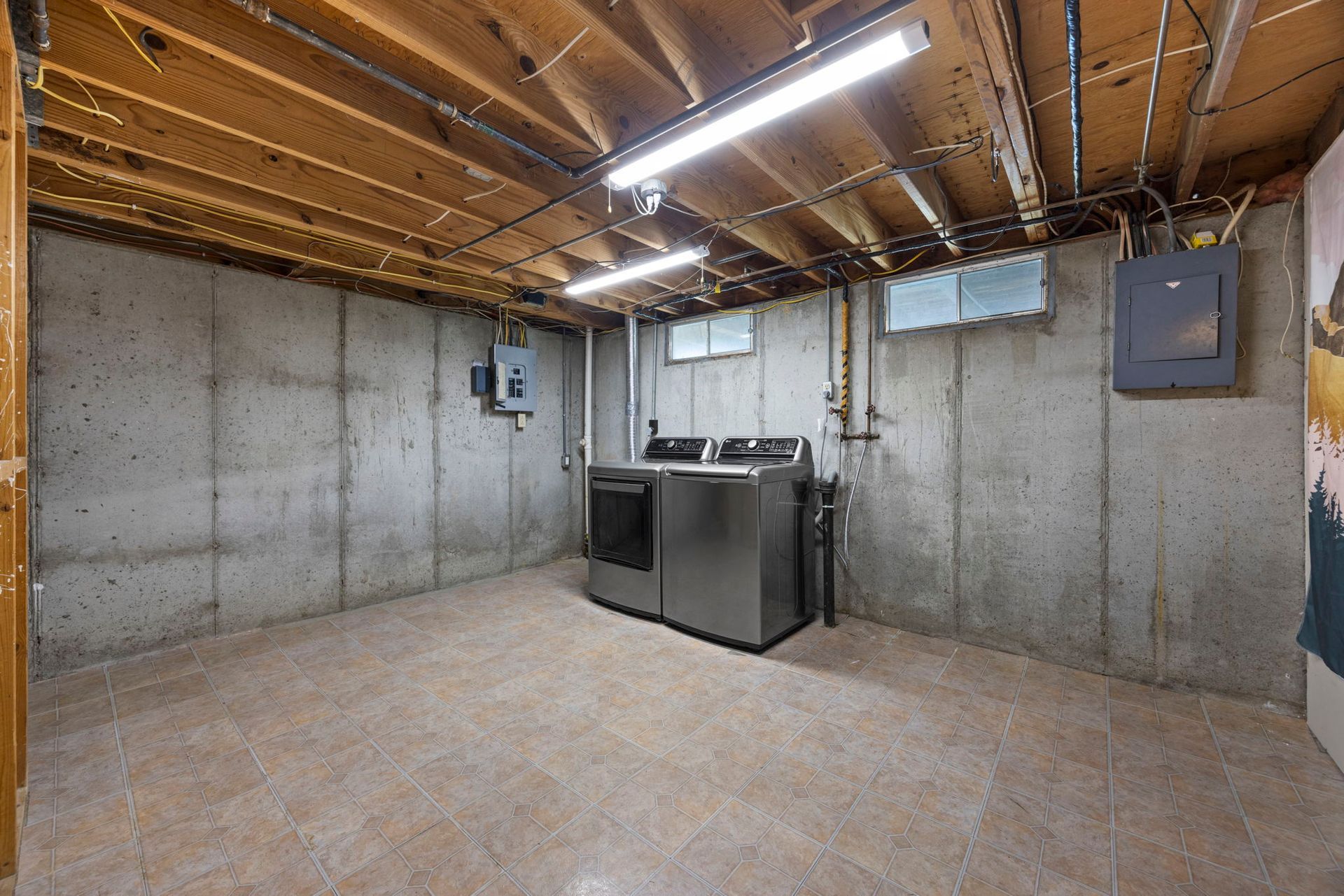 Basement laundry room with a washer/dryer, concrete walls, and exposed ceiling beams.