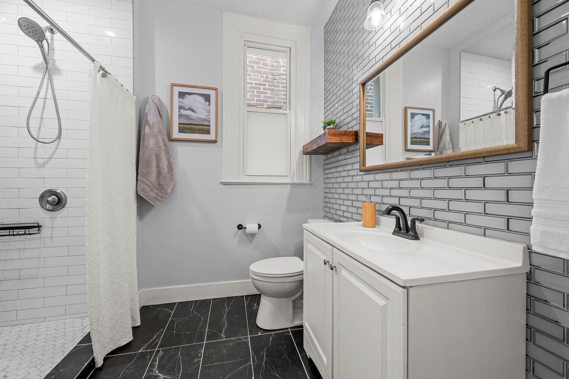 Bathroom with white tile shower, gray walls, black and white floor, white vanity, and gold-framed mirror.