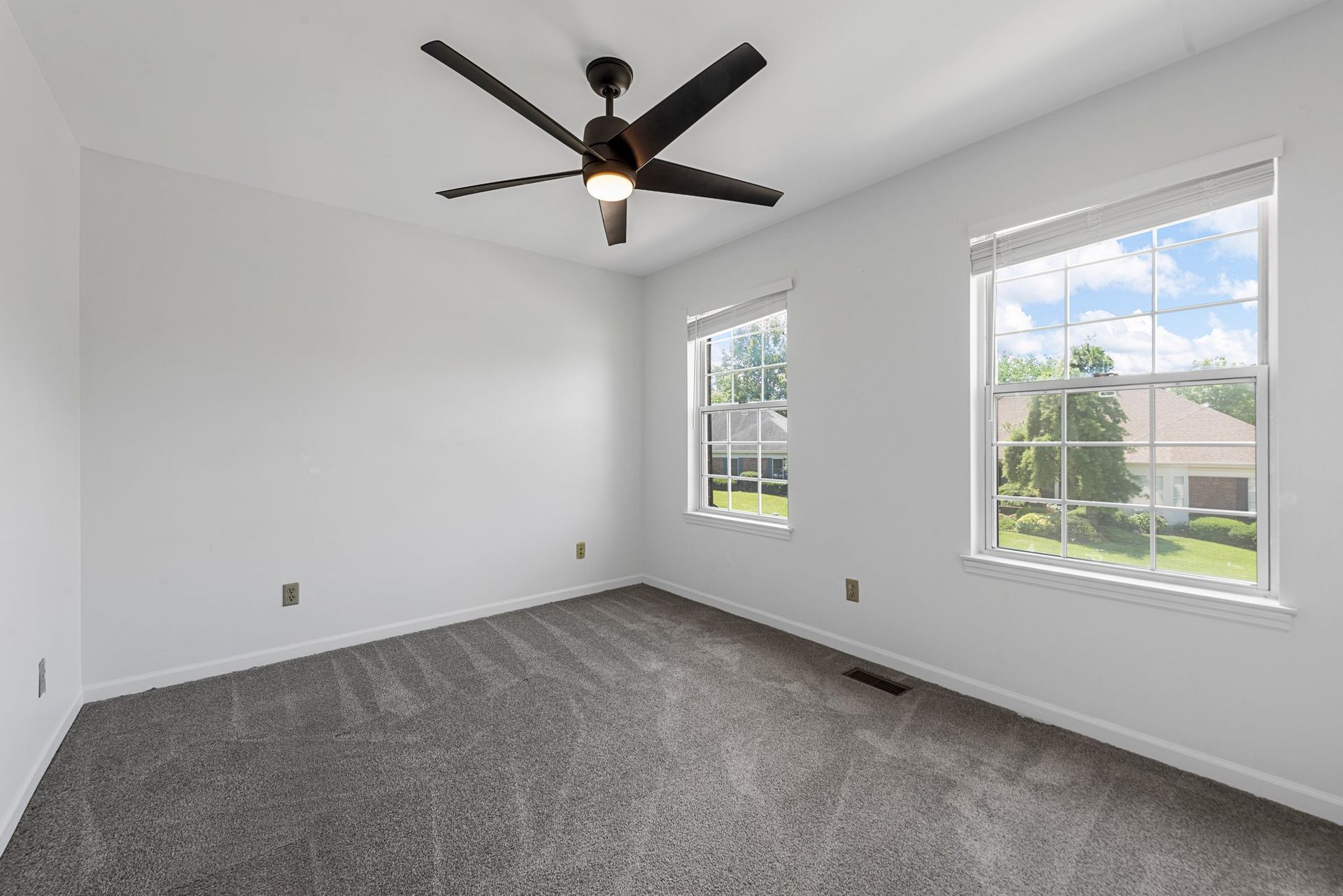 An empty bedroom with a ceiling fan and two windows.