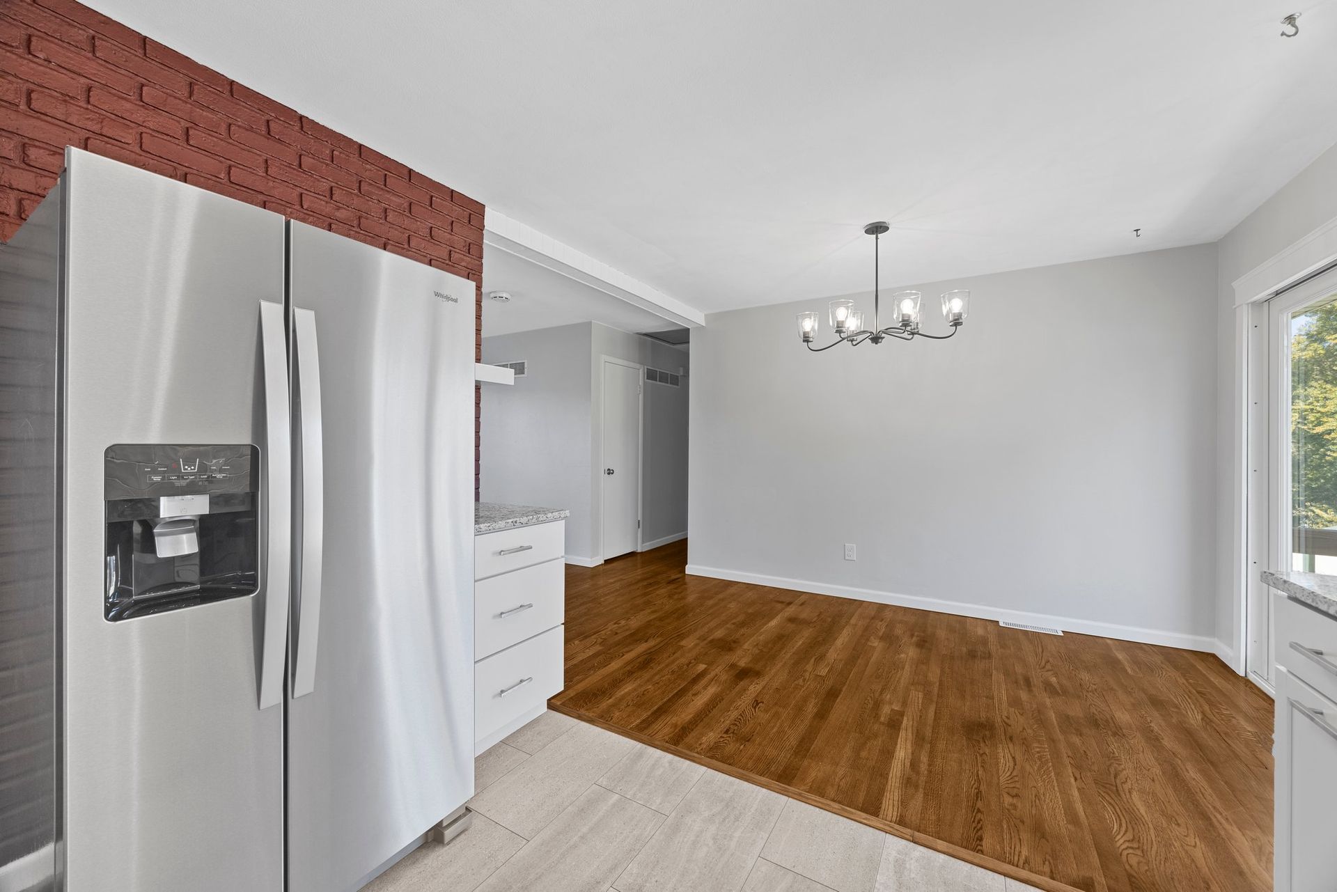 An empty kitchen with a stainless steel refrigerator and hardwood floors.