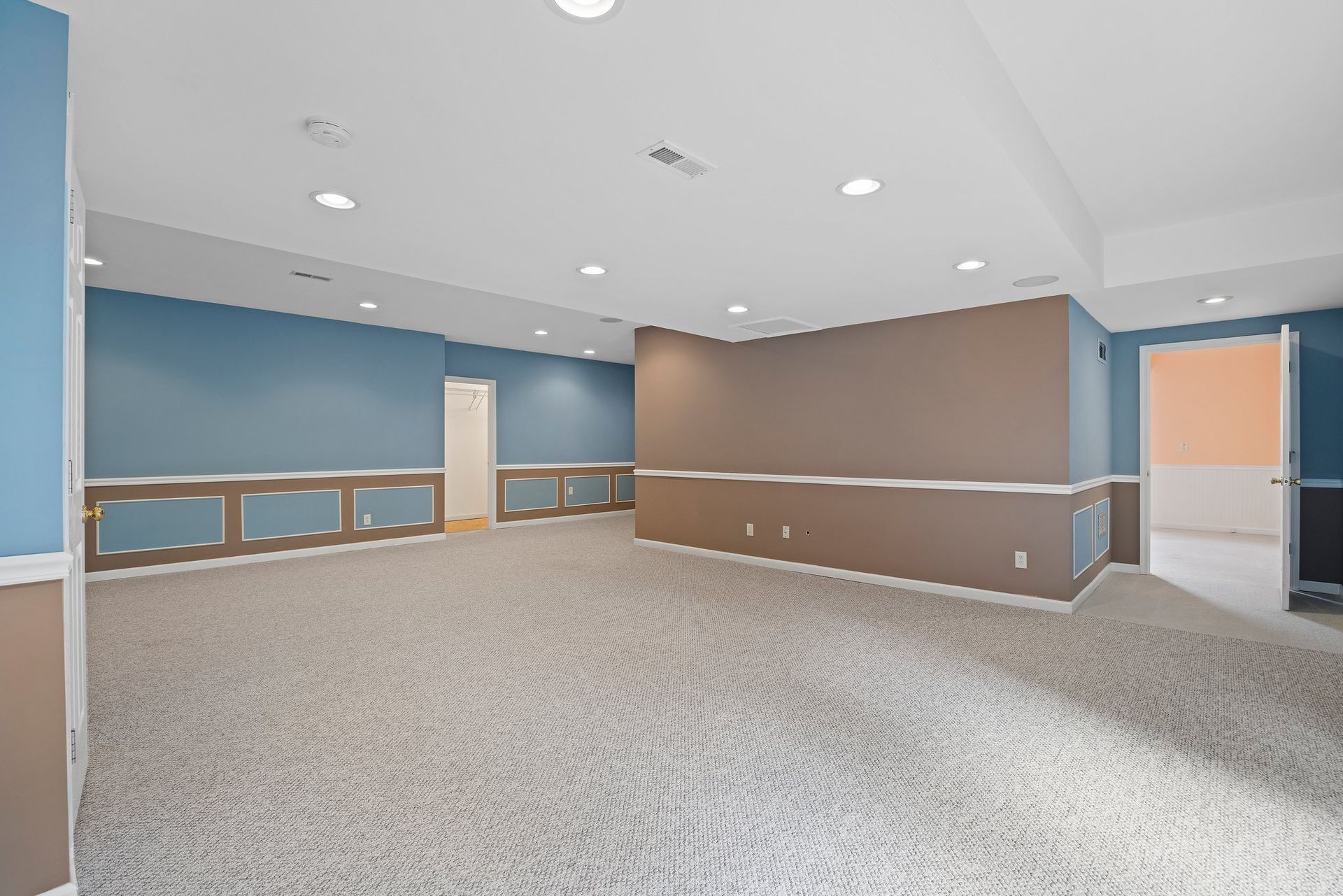 An empty basement with a carpeted floor and blue and brown walls.