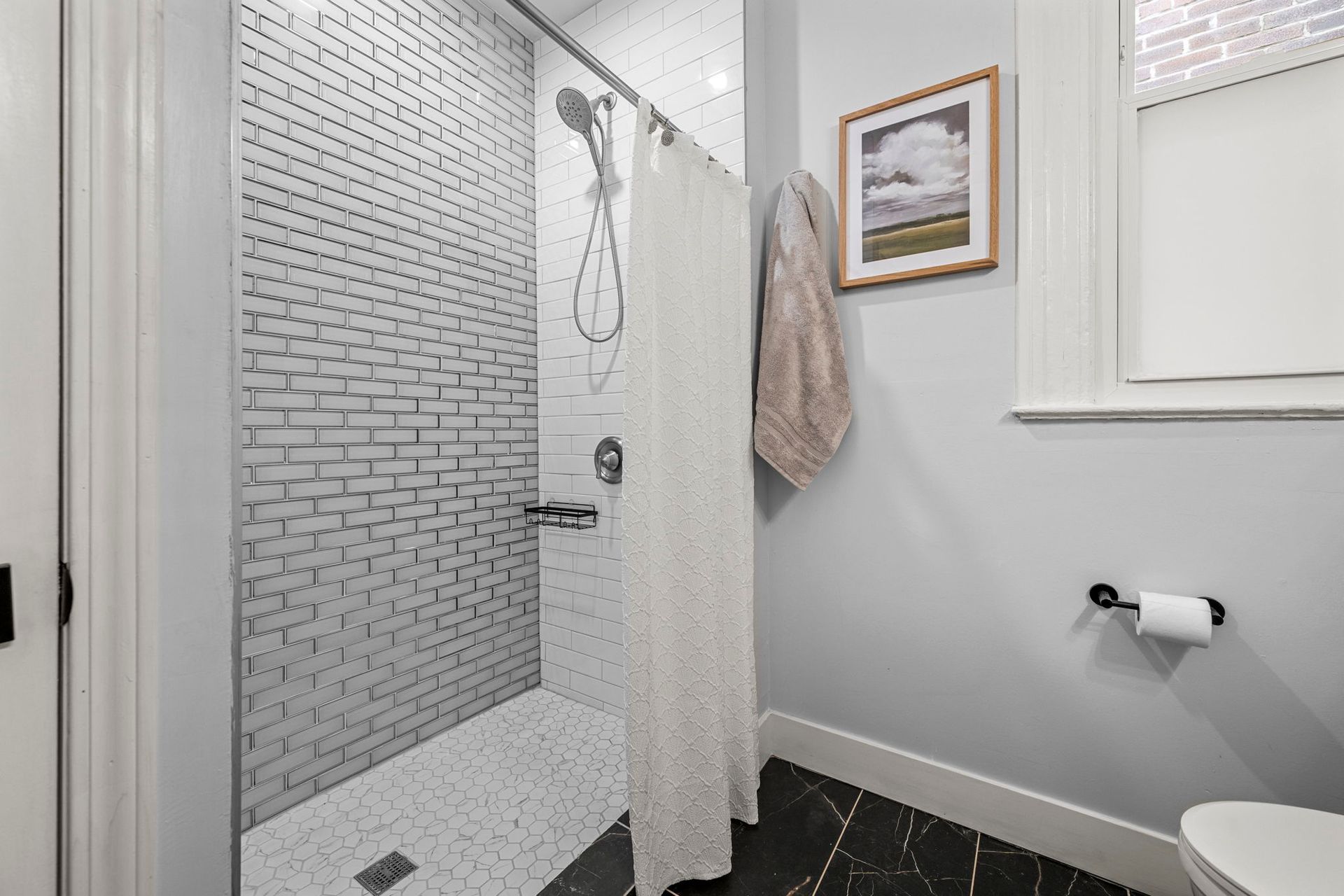 Small bathroom with tiled shower, light gray walls, black and white patterned floor, and a window.