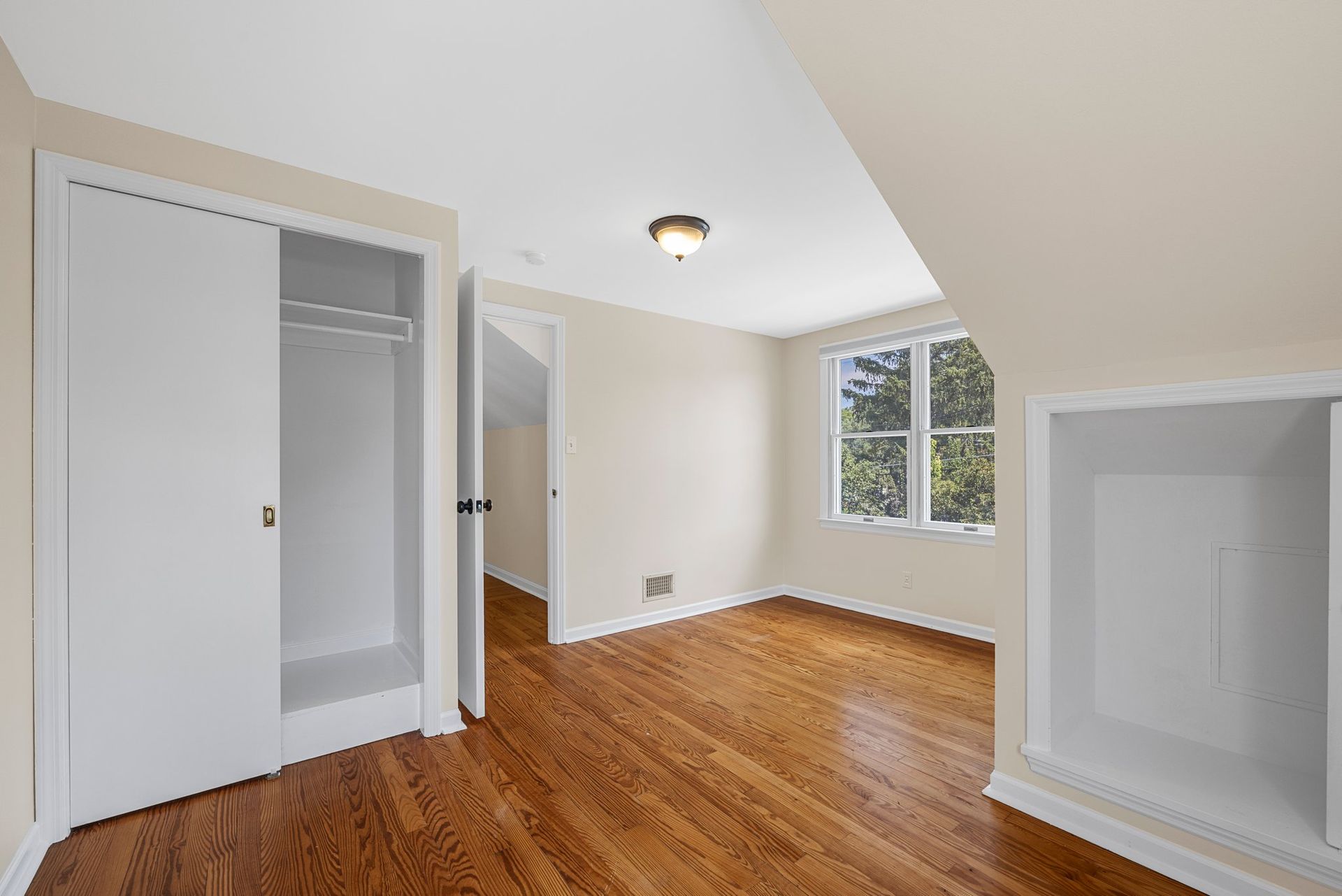 An empty bedroom with hardwood floors and white walls.