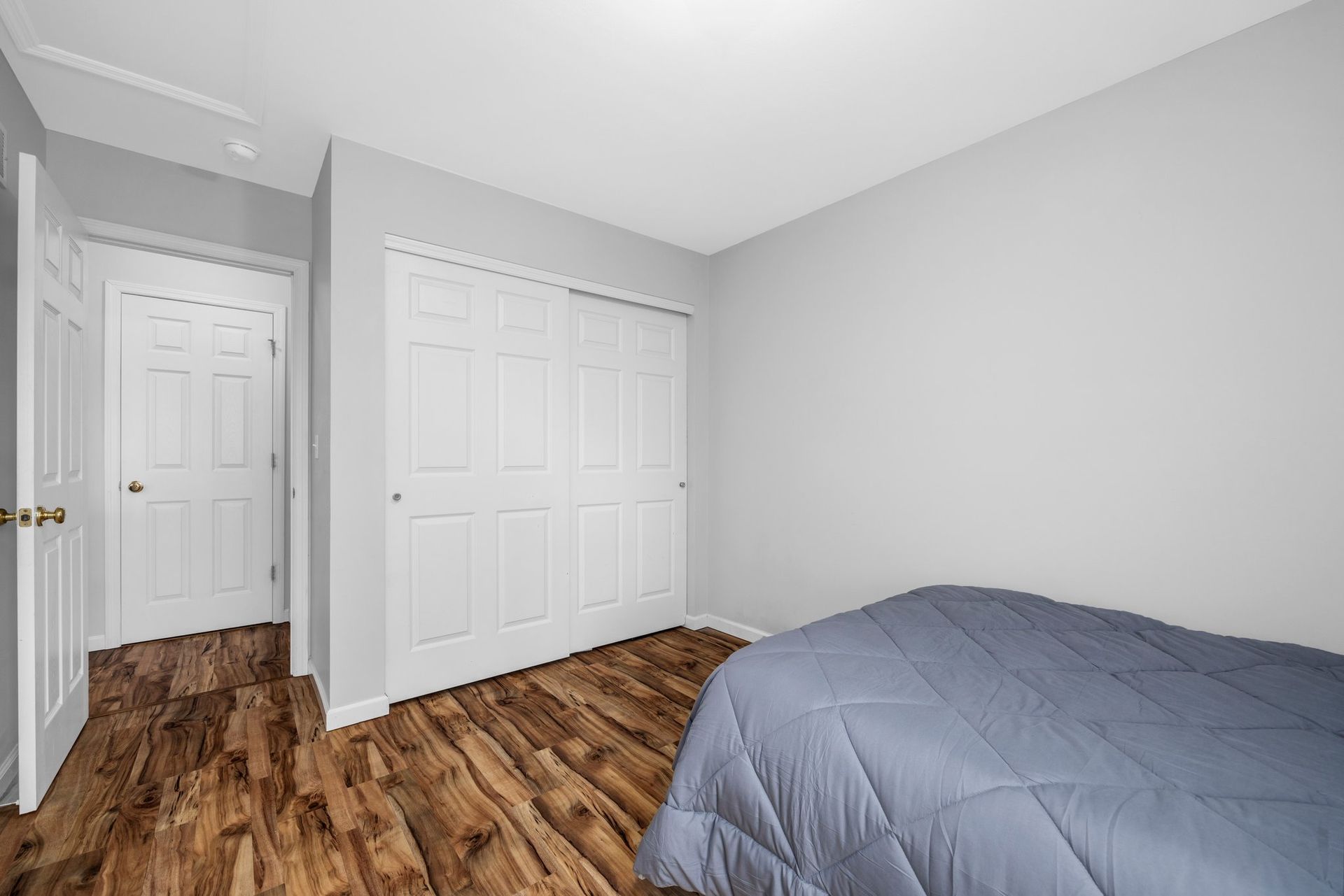 A bedroom with a bed , closets and hardwood floors.