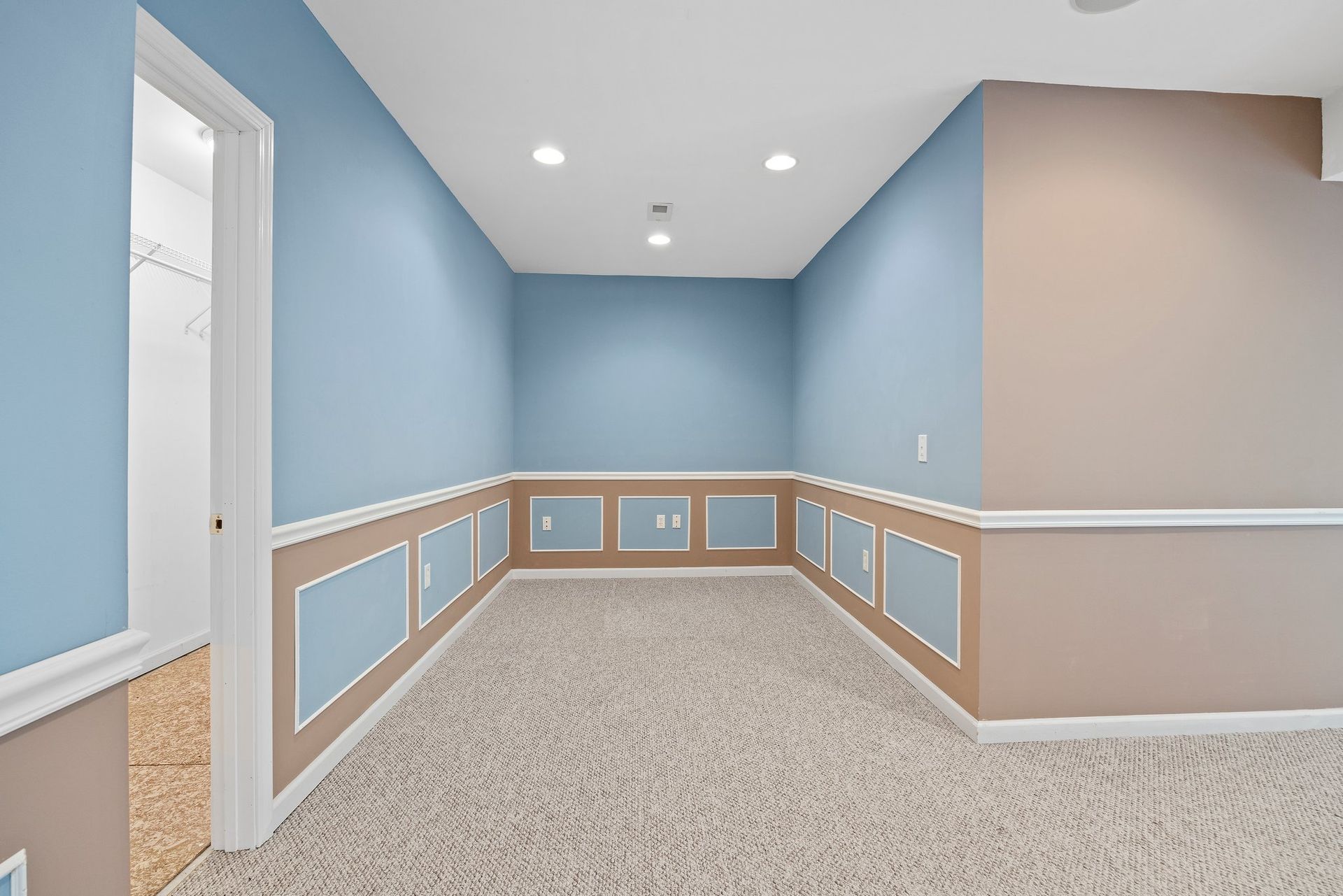An empty room with blue and tan walls and a carpeted floor.