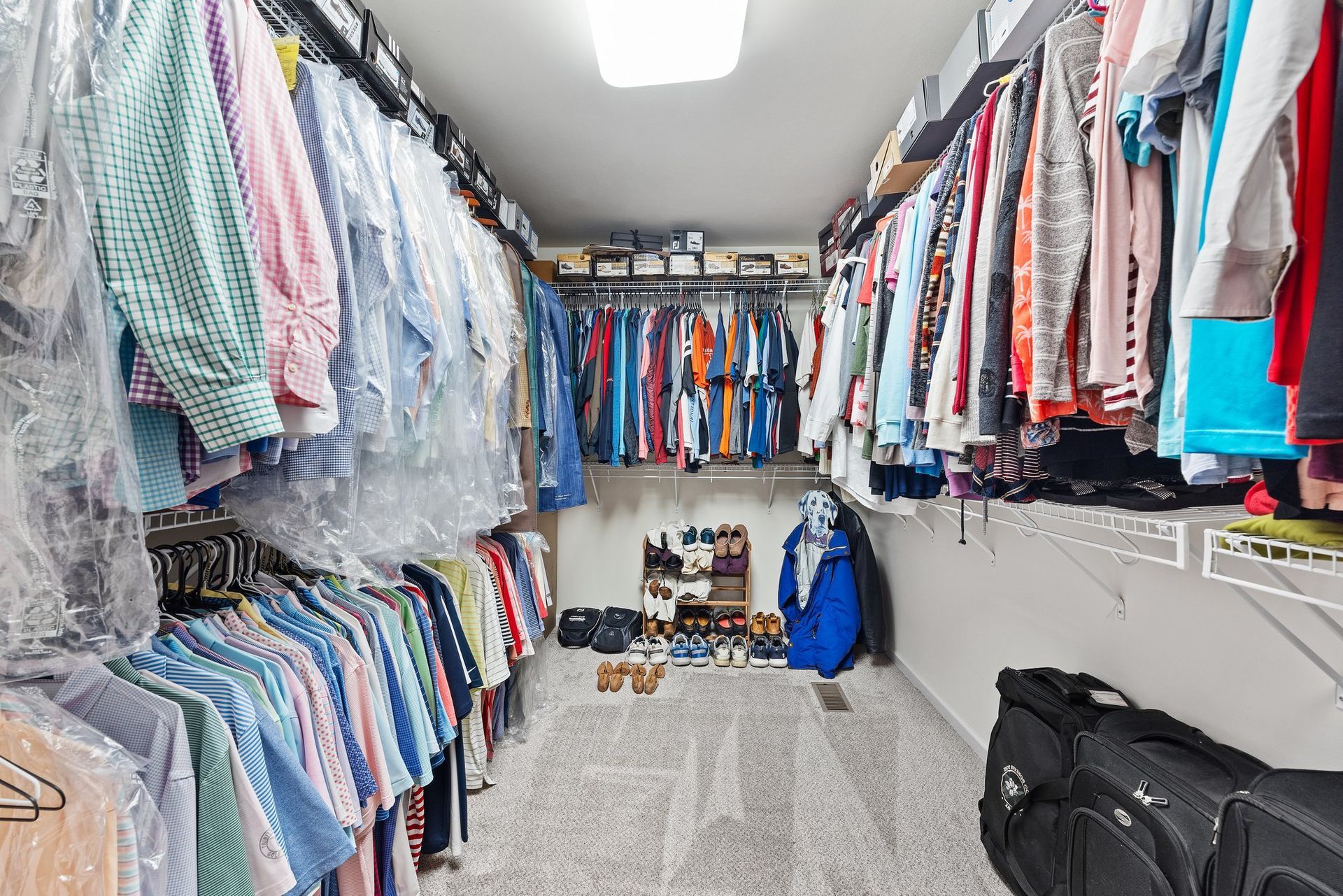 A walk in closet filled with lots of clothes and a suitcase.