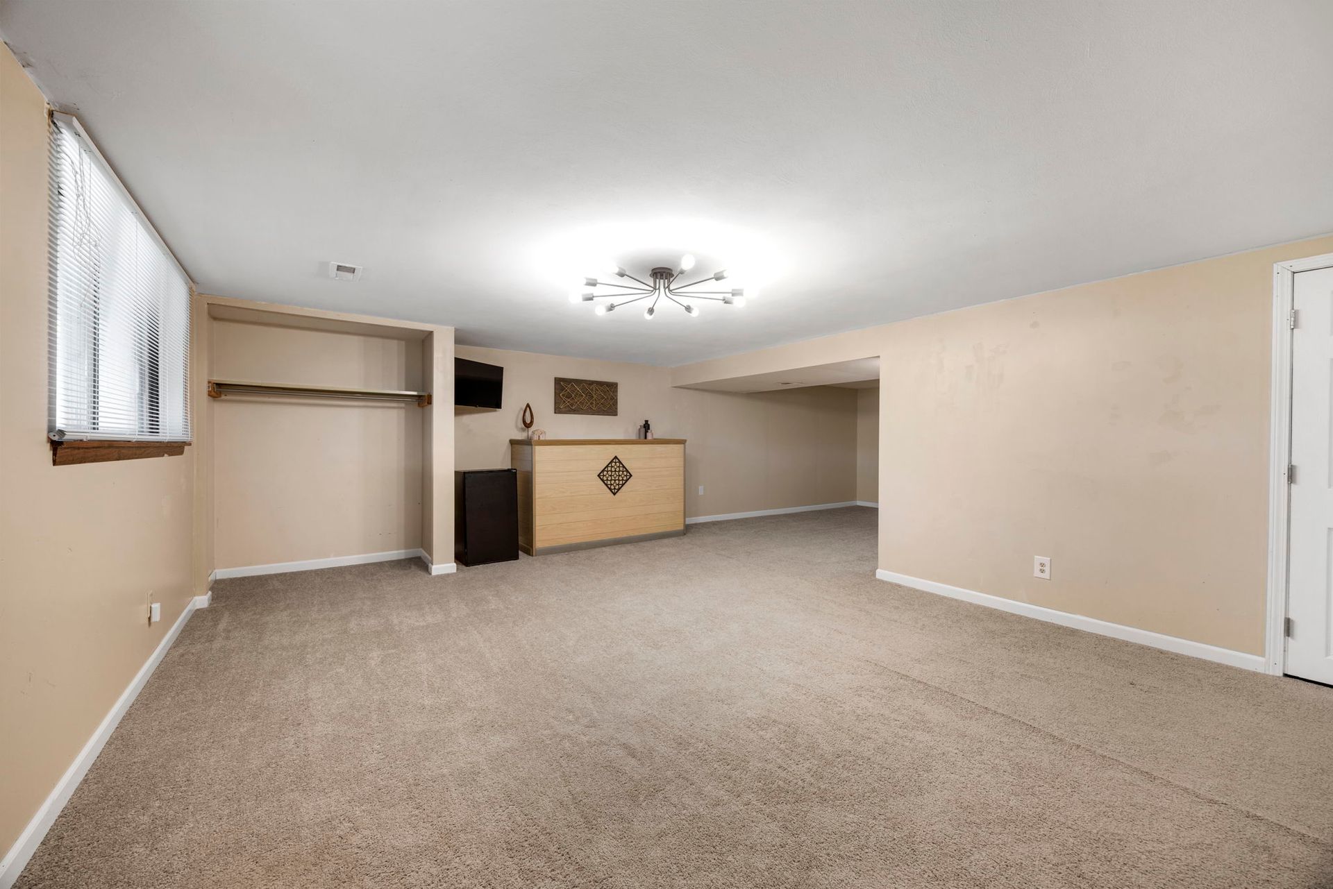 Empty finished basement with carpet, bar, and window.