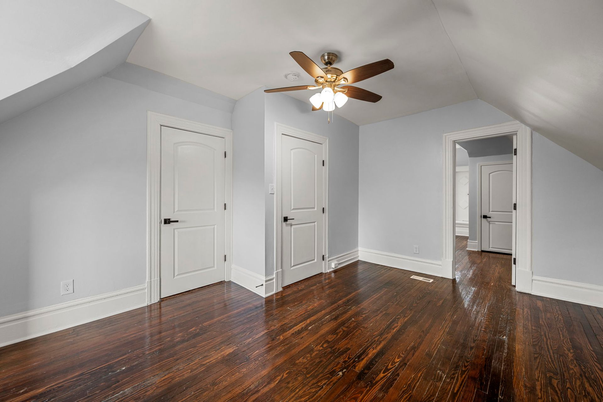 Bedroom with hardwood floors, light blue walls, white doors, and a ceiling fan.