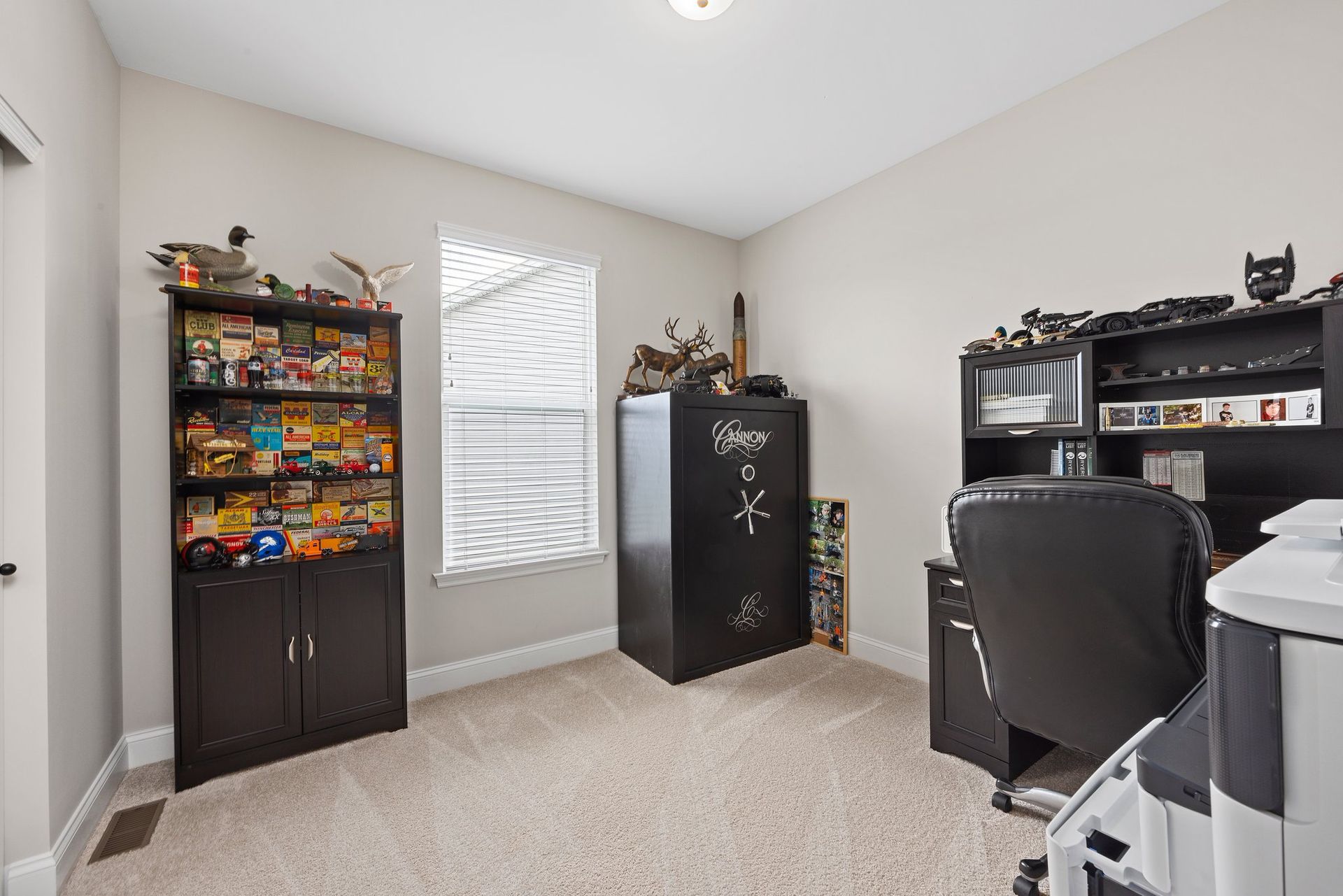 A room with a desk , chair , bookshelf , safe and printer.