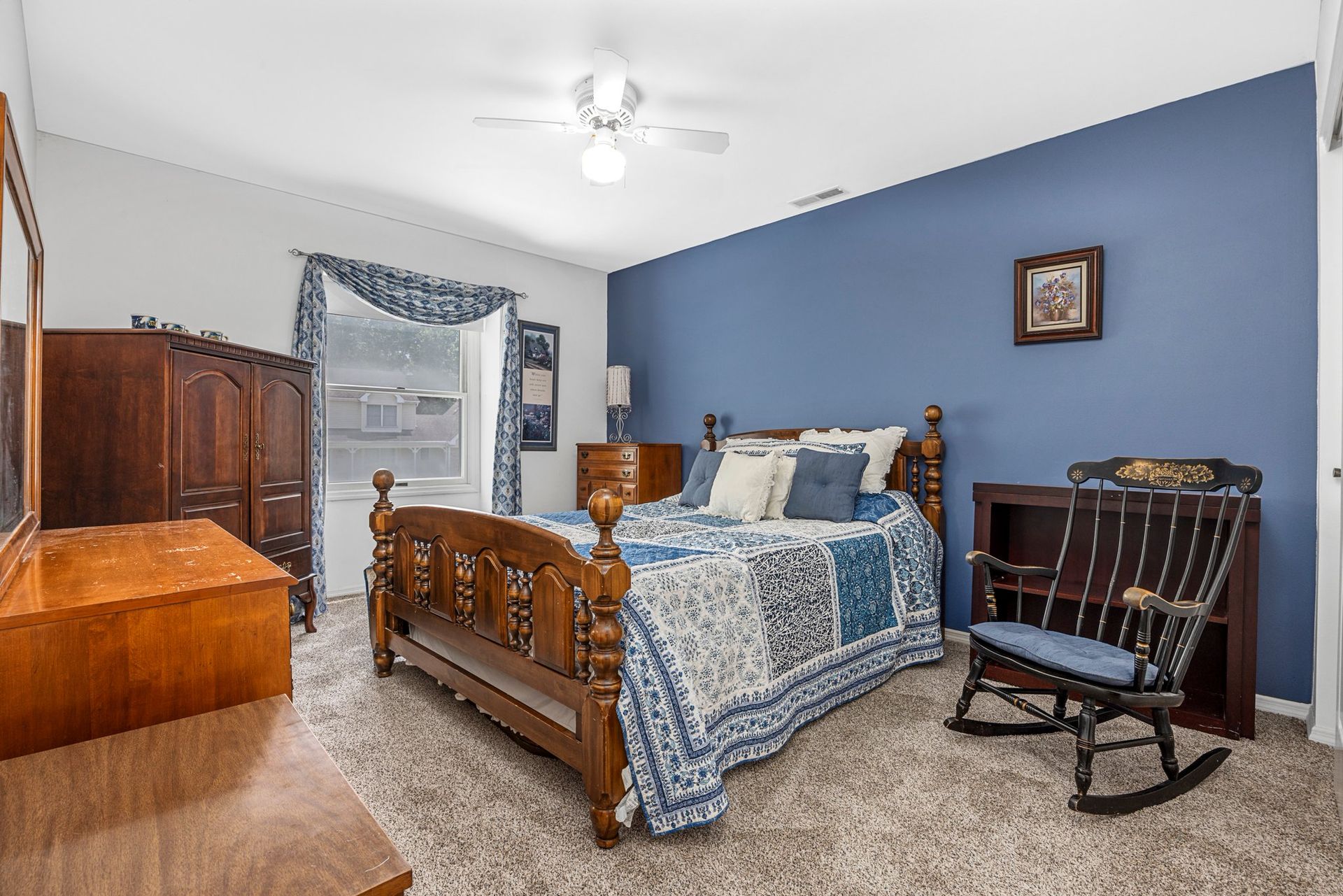 A bedroom with a bed , rocking chair , dresser , mirror and blue walls.