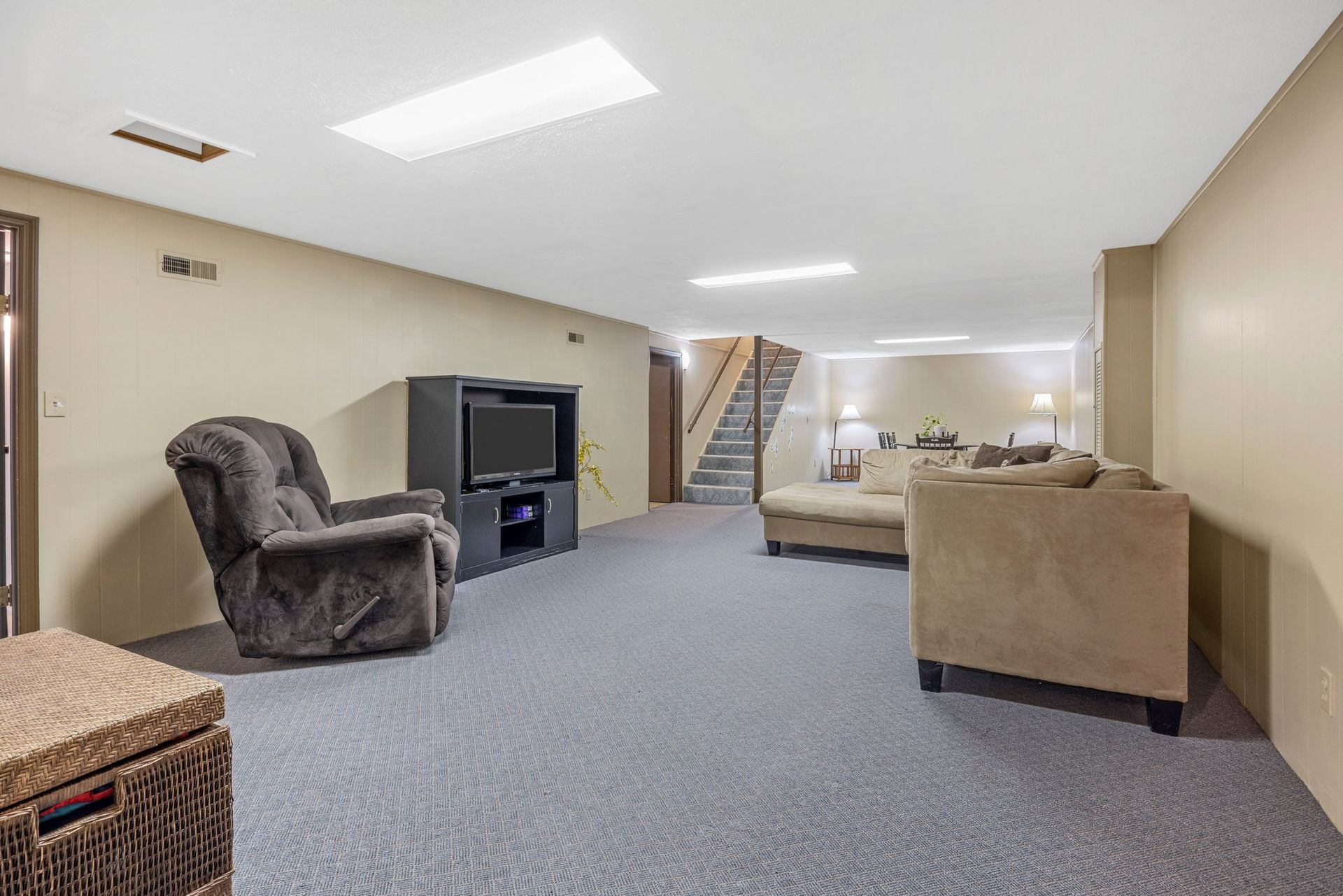 A living room with a couch , chair , television and stairs.