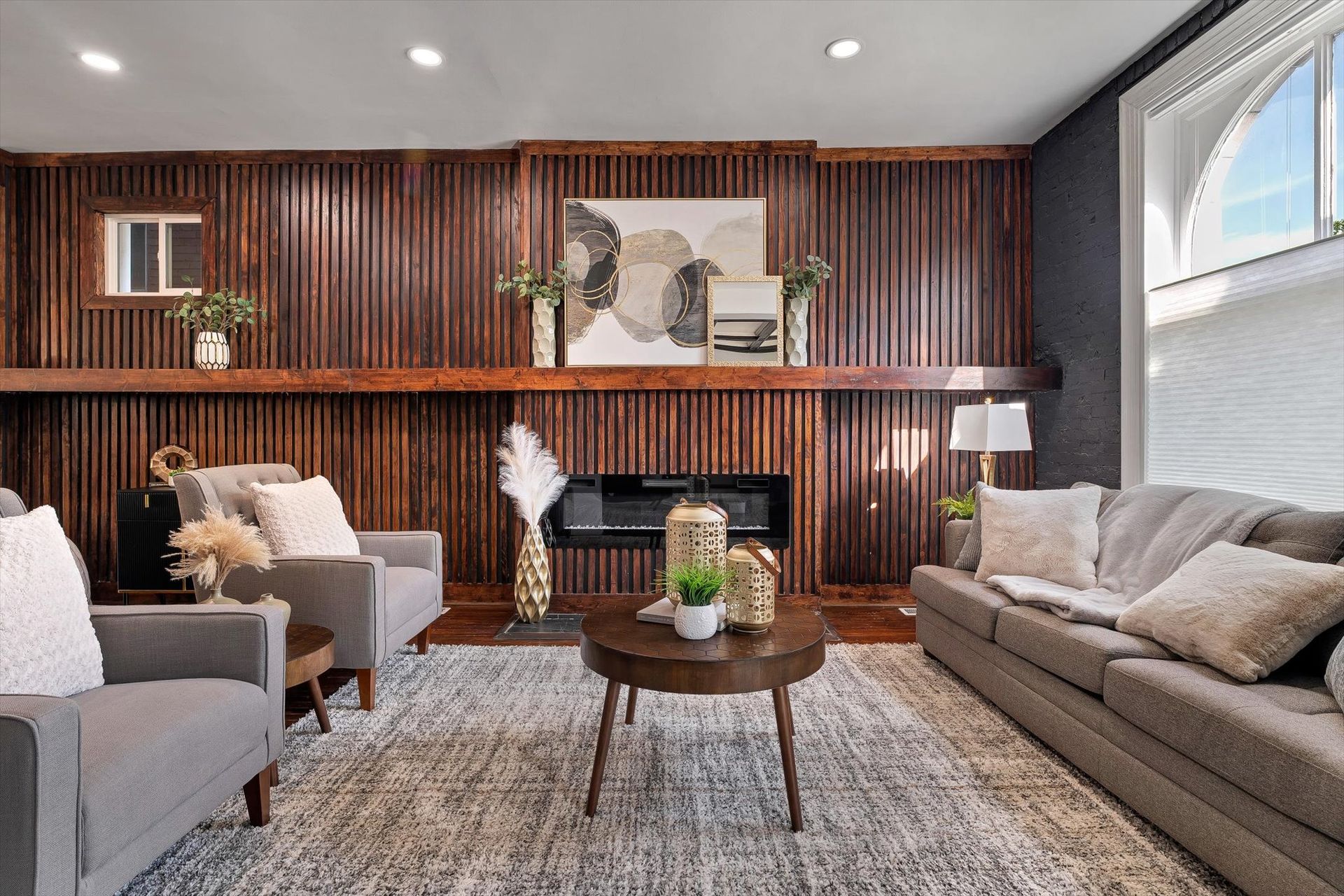 Living room with gray furniture, wooden accent wall, fireplace, and area rug.
