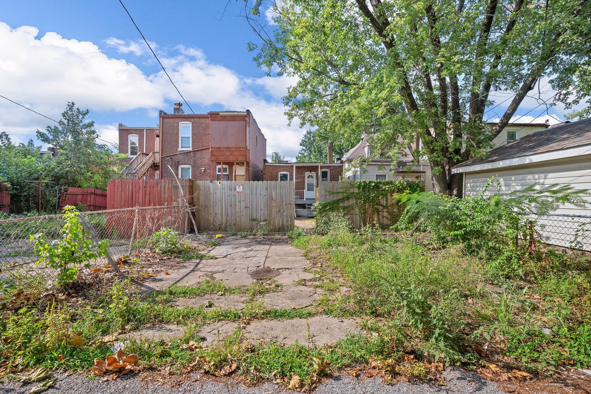An empty backyard with a fence and a brick building in the background.