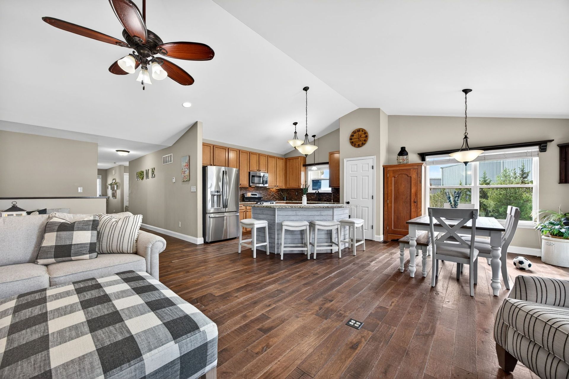Open-concept home featuring a living area with a plaid ottoman, a kitchen with an island, and a dining space.
