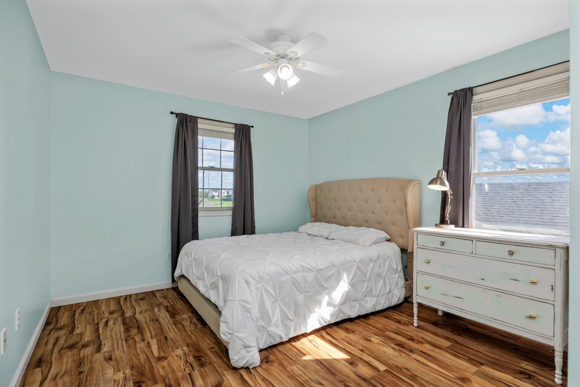A bedroom with a bed , dresser , window and ceiling fan.