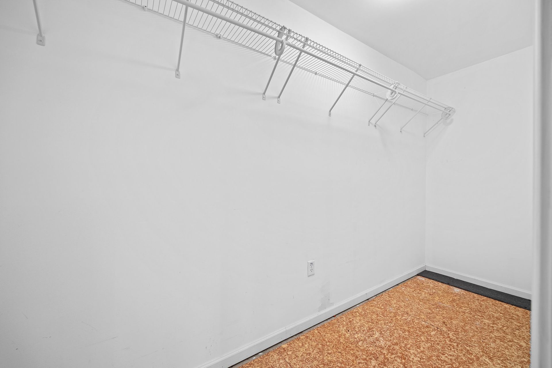 An empty walk in closet with a carpeted floor and a white wall.