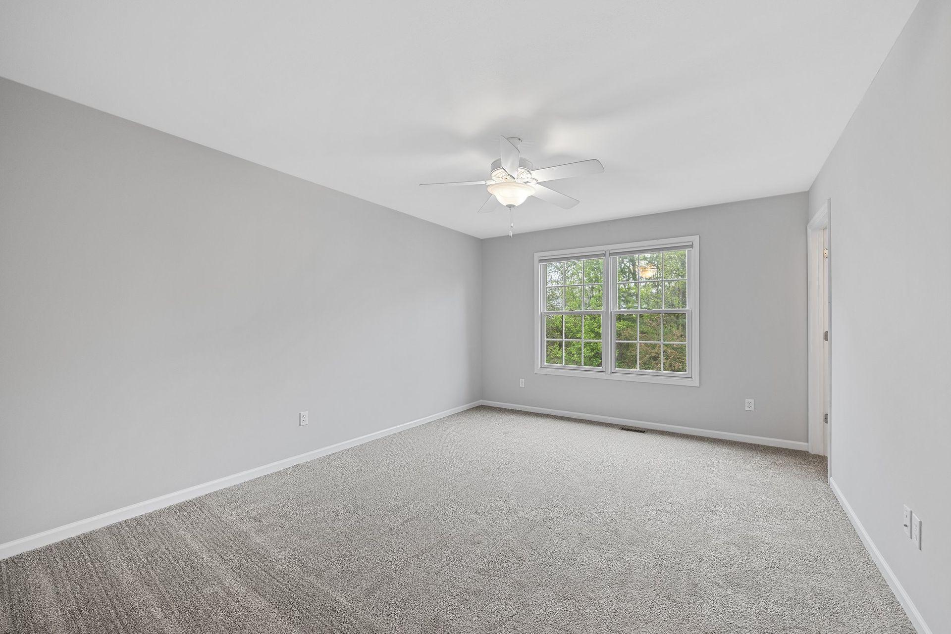 An empty bedroom with a ceiling fan and two windows.