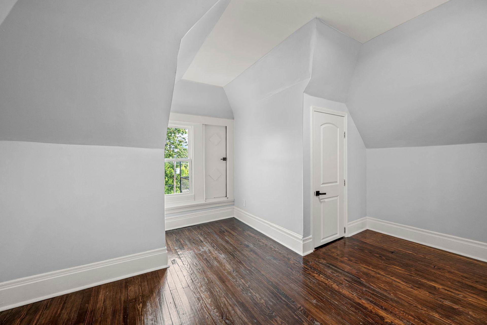 Empty attic room with hardwood floors, white trim, and light blue walls.