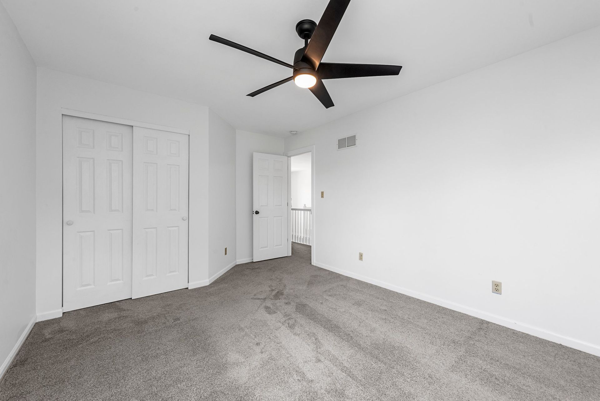 An empty bedroom with a ceiling fan and a gray carpet.