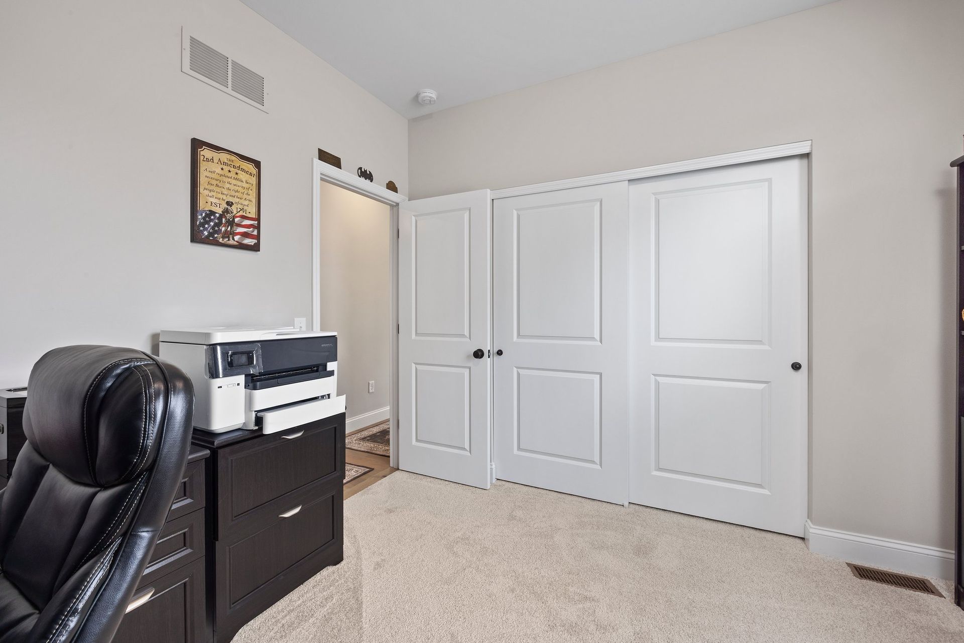 A room with a desk , chair , printer and closet.