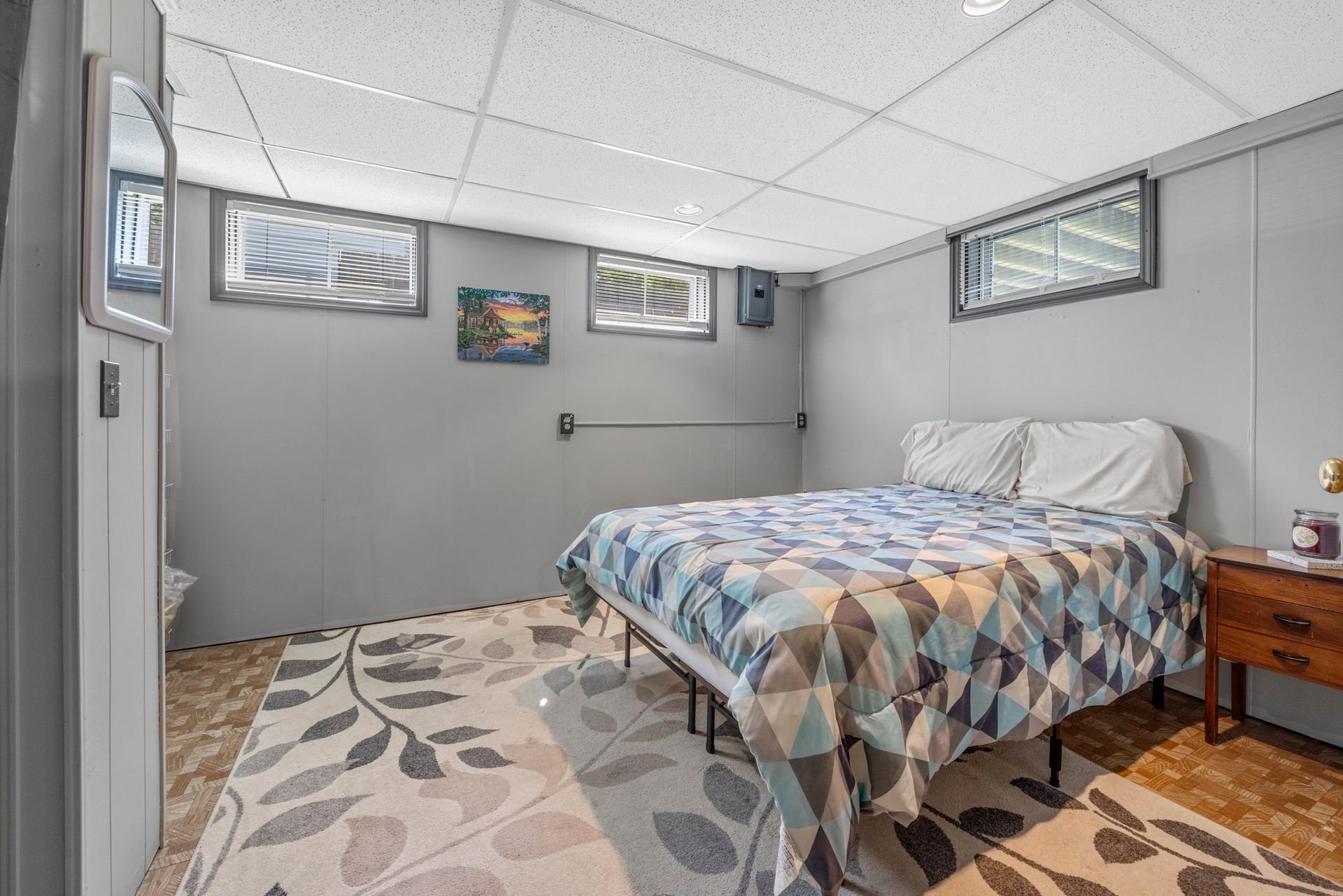 A bedroom with a bed , nightstand , rug and windows.