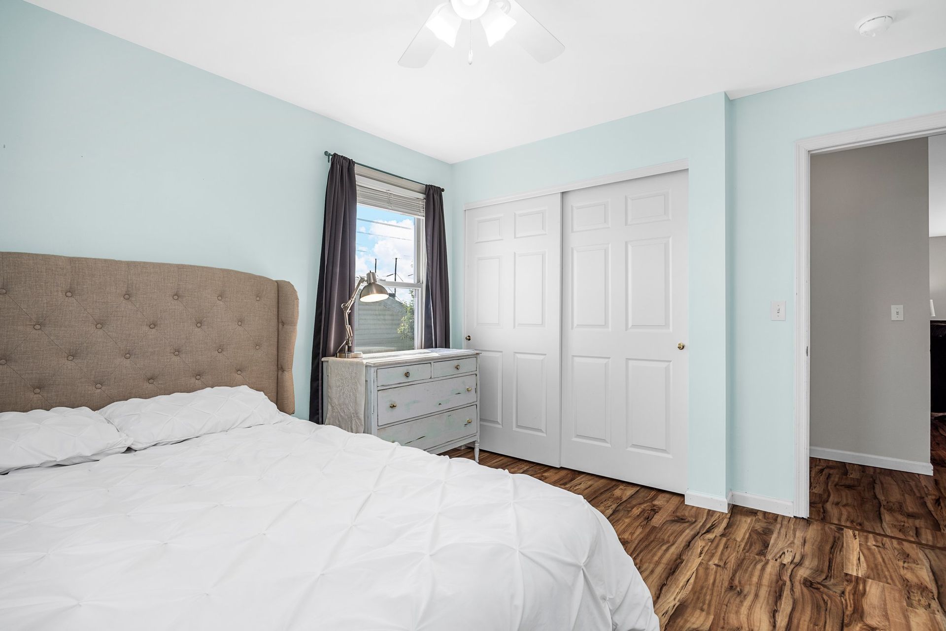 A bedroom with a bed , dresser , window and hardwood floors.
