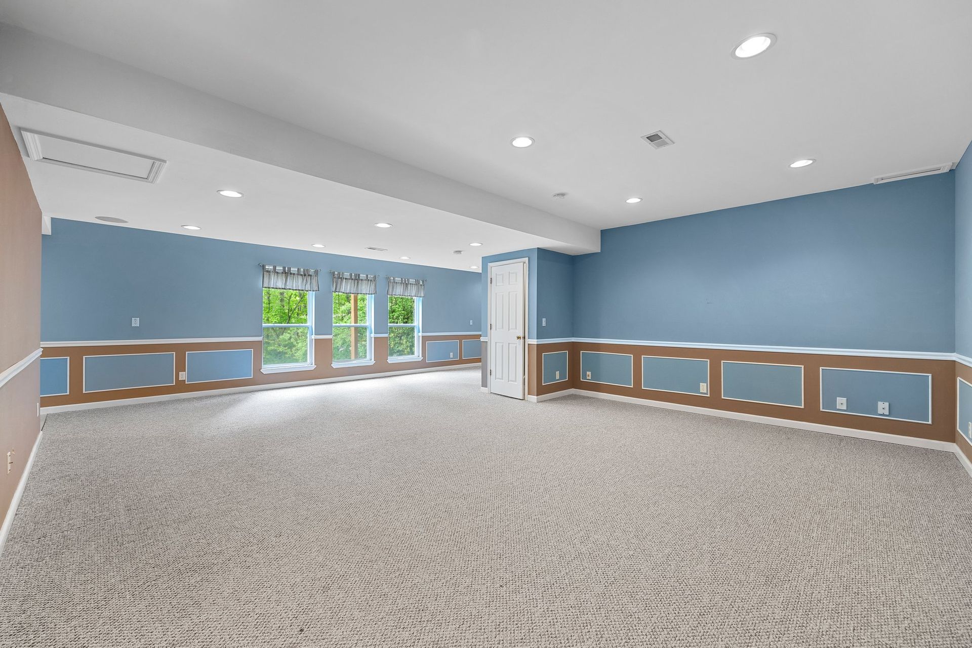 An empty basement with blue walls and a carpeted floor.