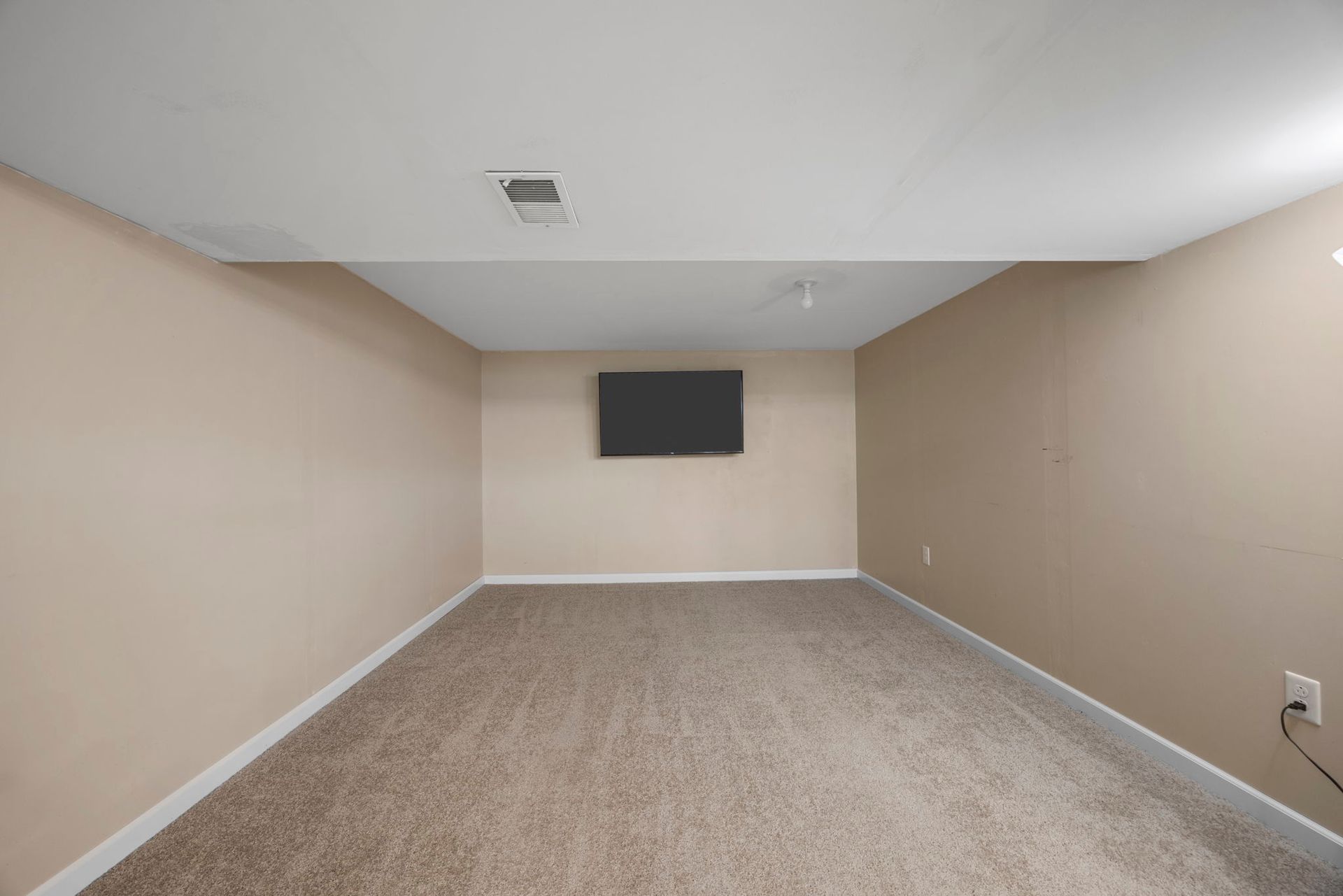 Empty room with tan walls, carpet, and a mounted TV.