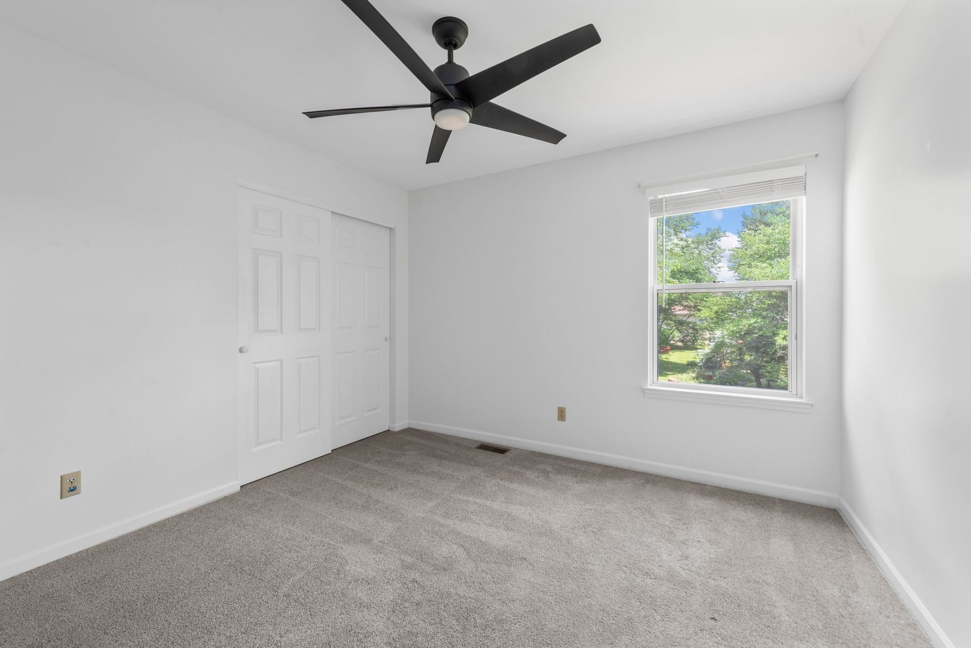 An empty bedroom with a ceiling fan and a window.