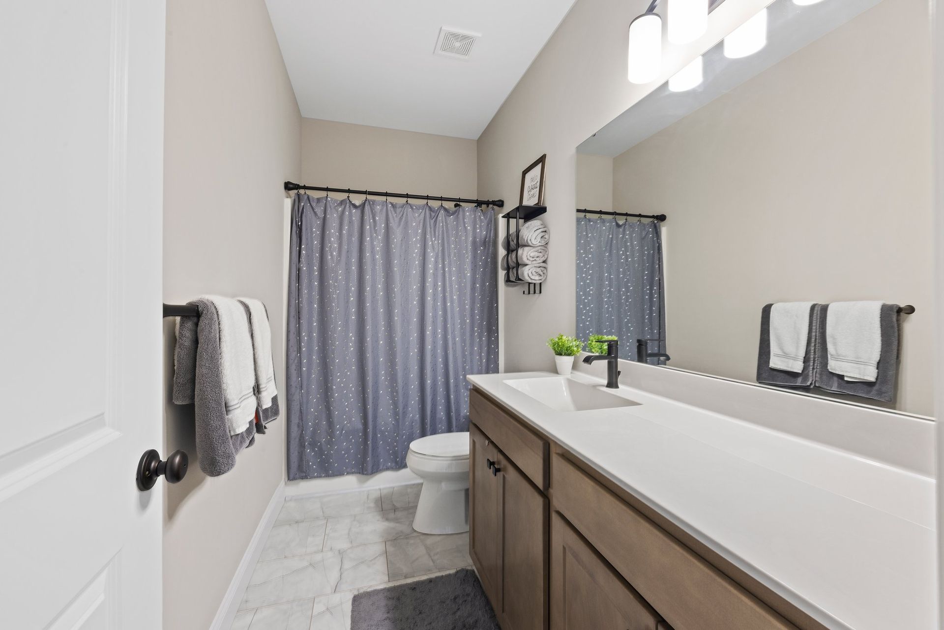A bathroom with a toilet , sink , mirror and shower curtain.