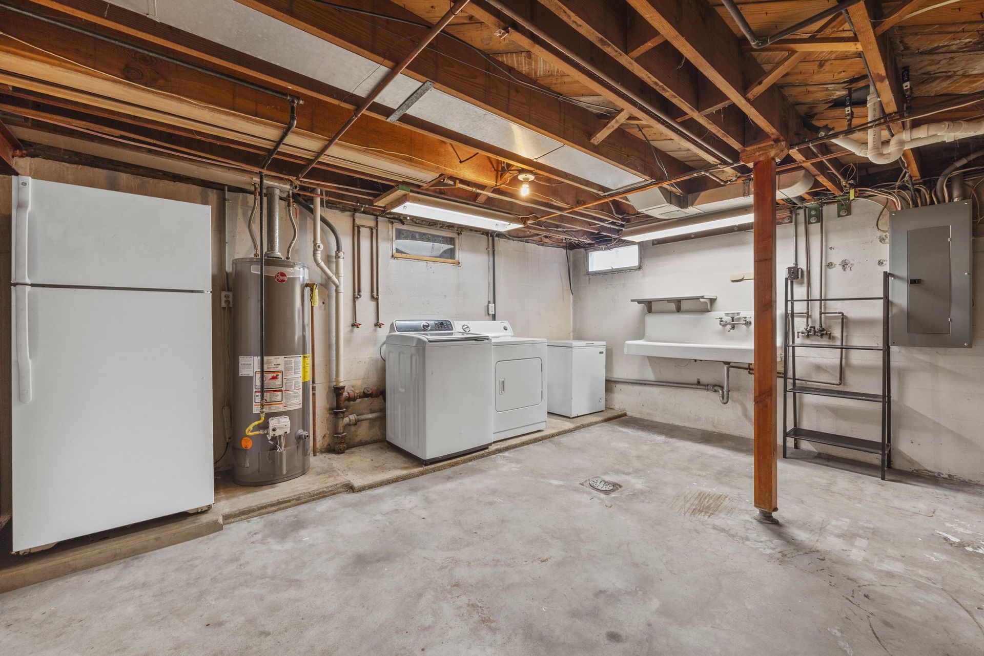 A basement with a washer and dryer , refrigerator , water heater and sink.