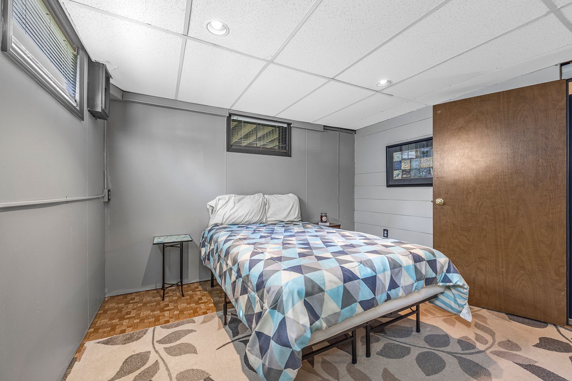 A bedroom in a basement with a bed and a rug.