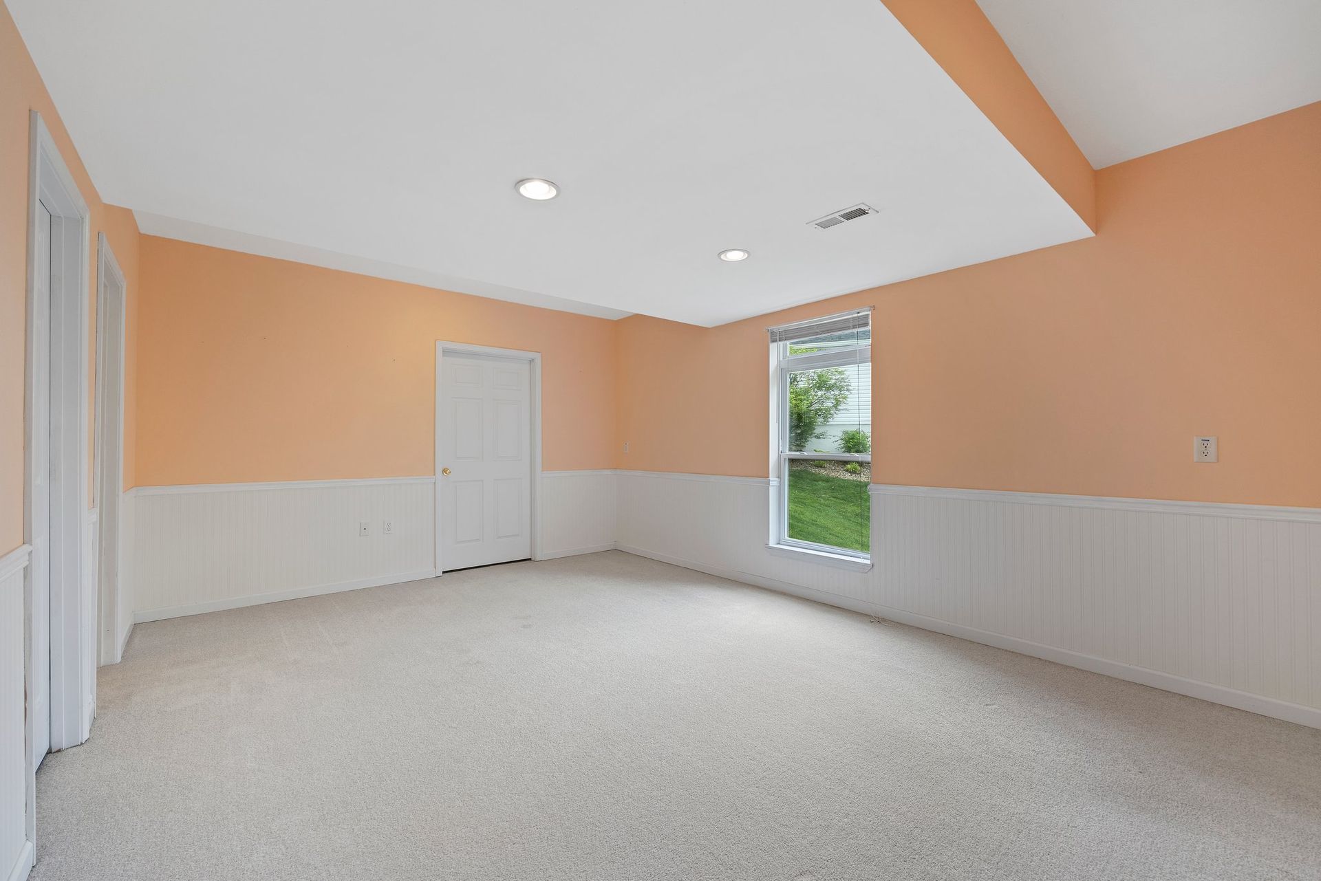 An empty room with orange walls and white trim and a window.